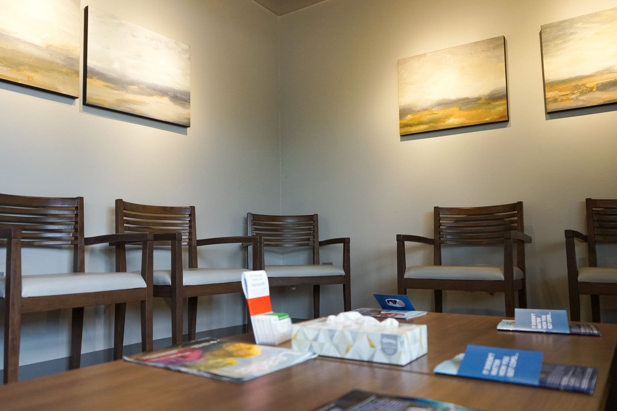 a waiting room with chairs , a table , and paintings on the wall .