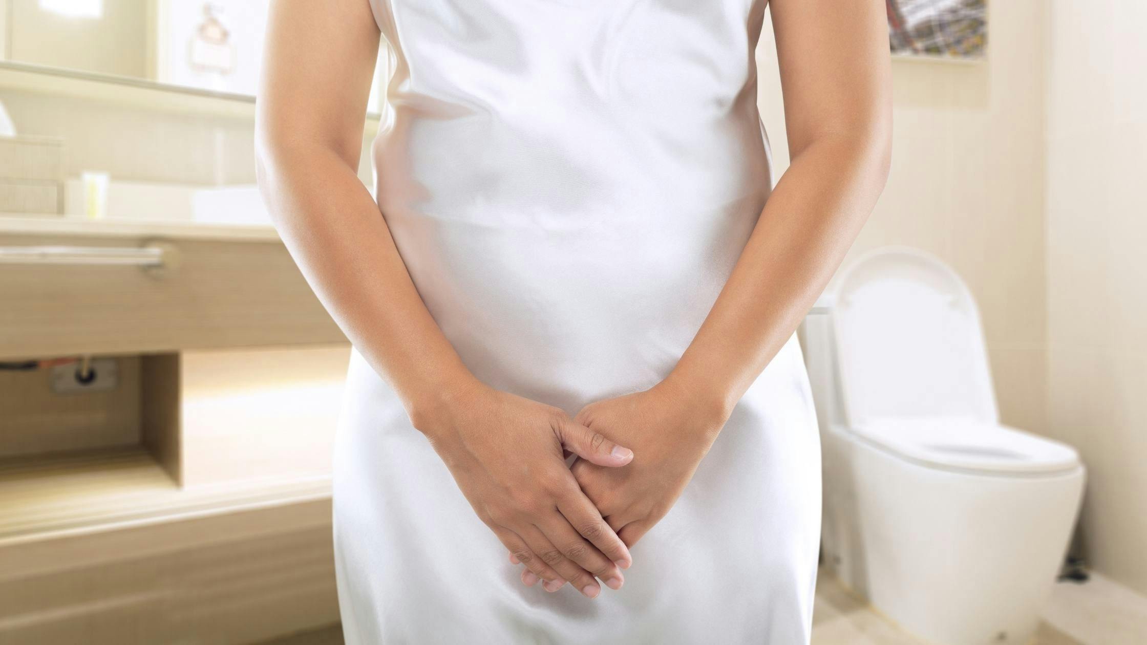 a woman in a white dress is standing in a bathroom with her hands on her stomach .