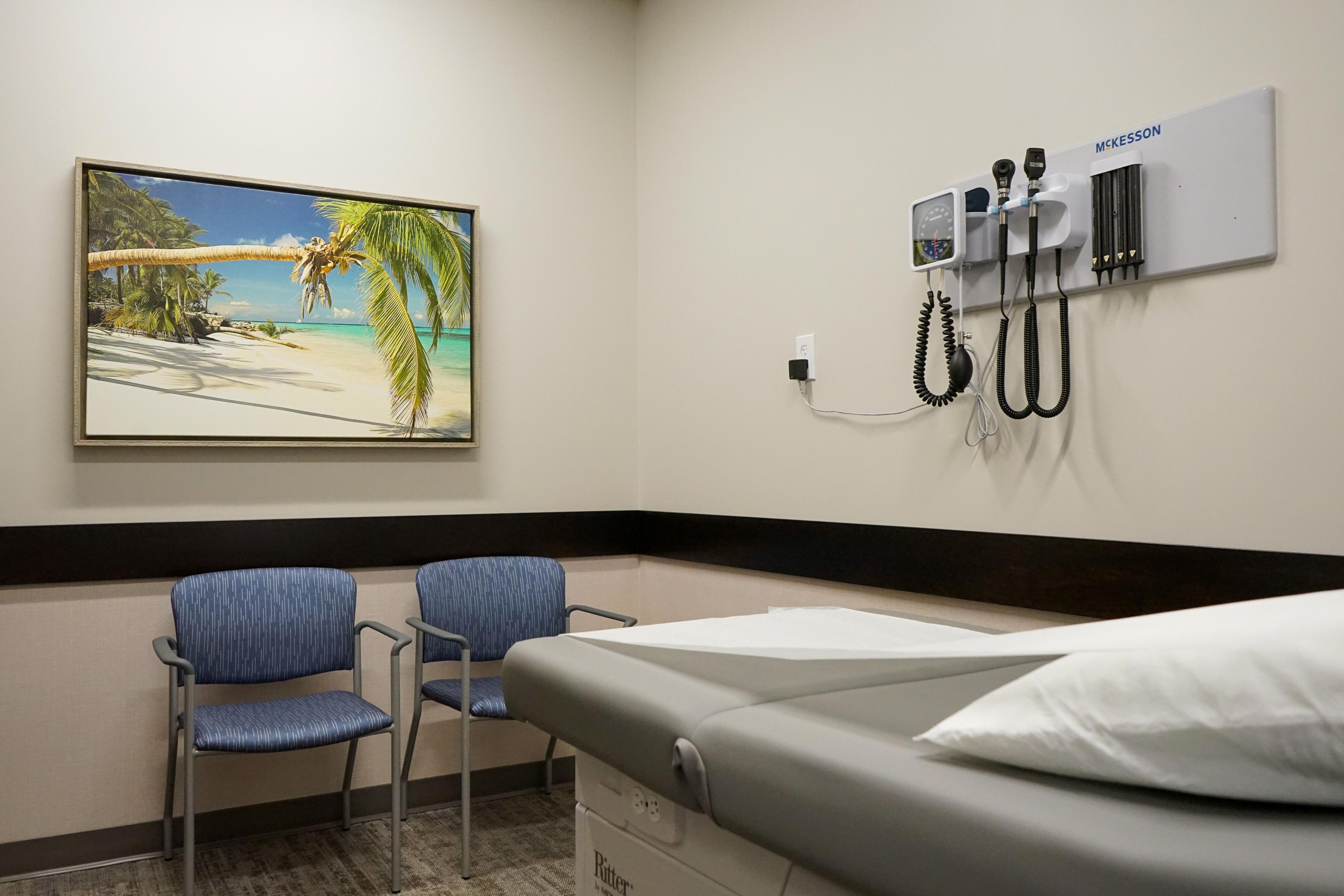 a doctor 's office with a bed , chairs , and a painting on the wall .