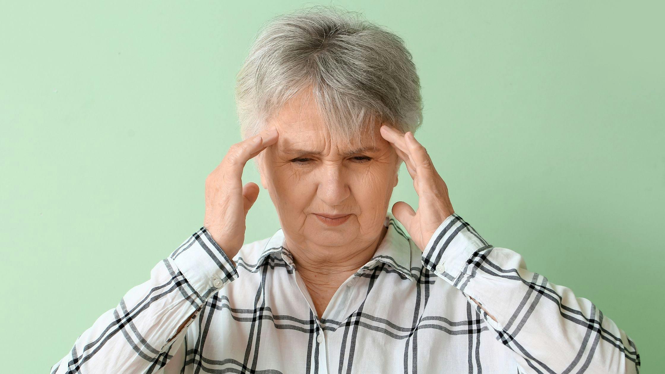 an elderly woman is holding her head because of a headache .