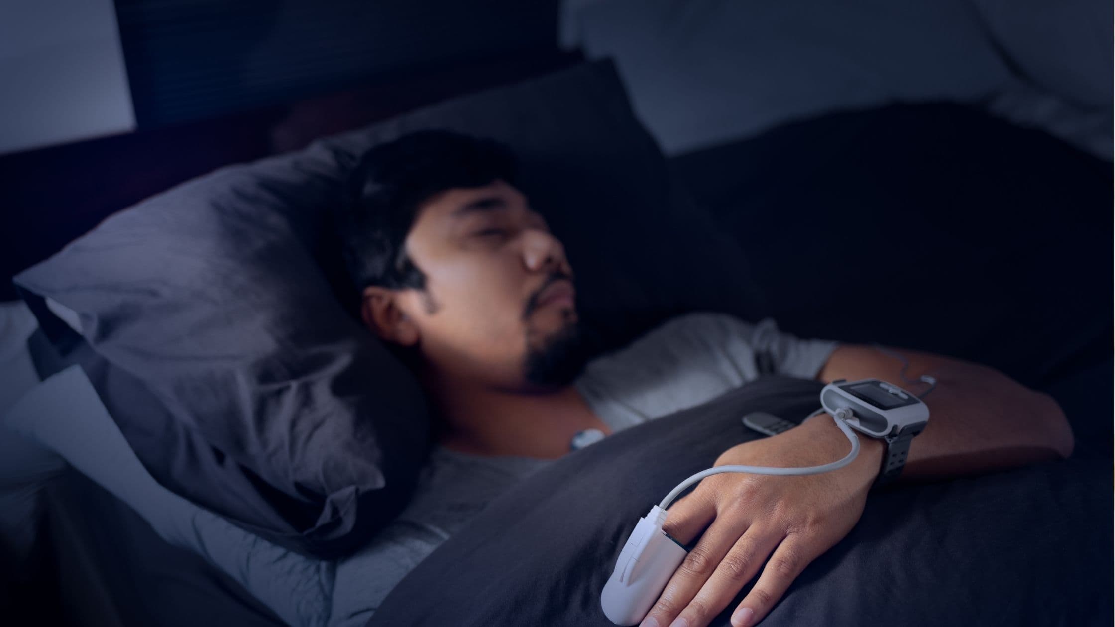 a man is sleeping in a bed with a pulse oximeter on his wrist .