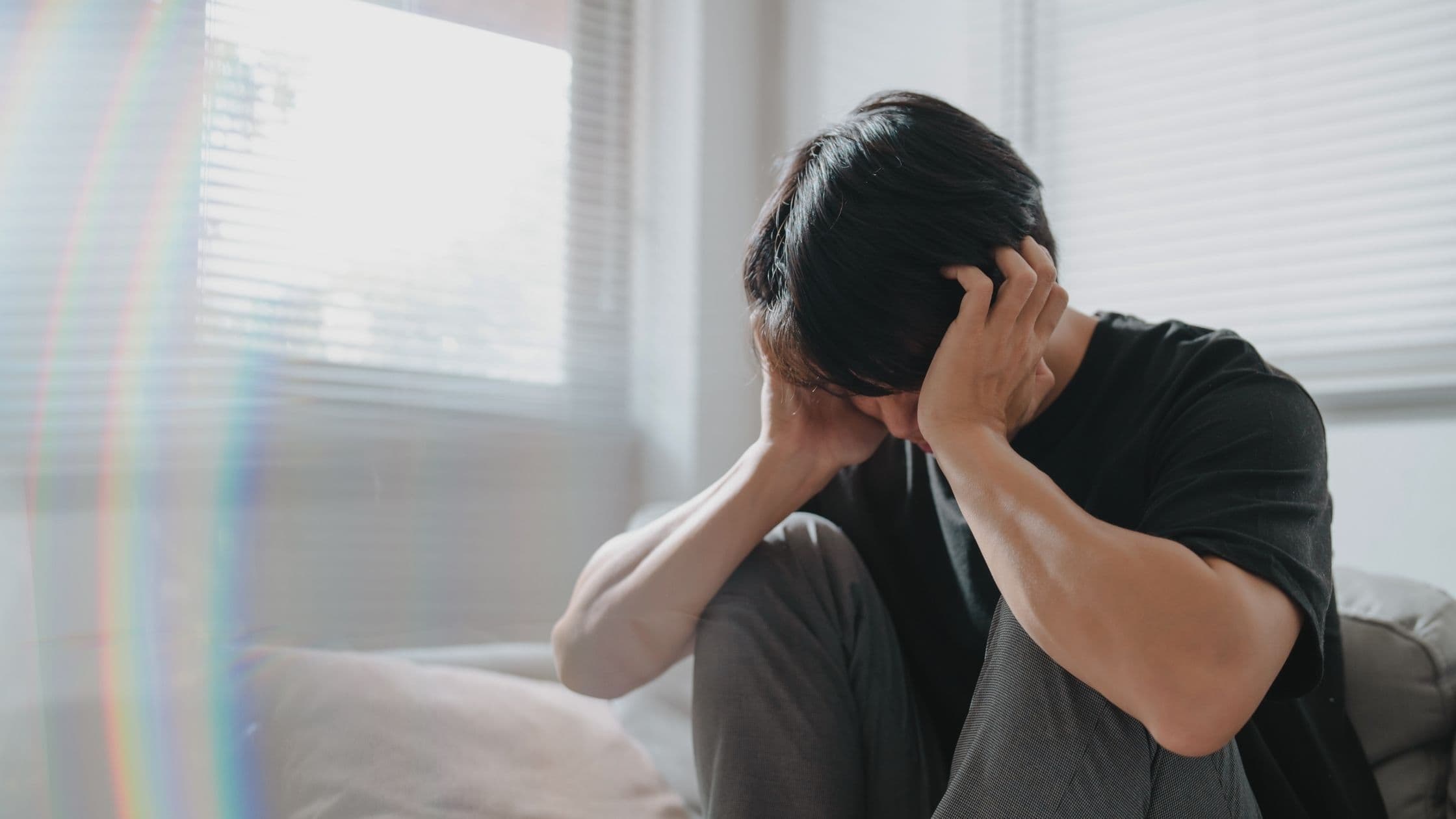 a man is sitting on a couch with his head in his hands .