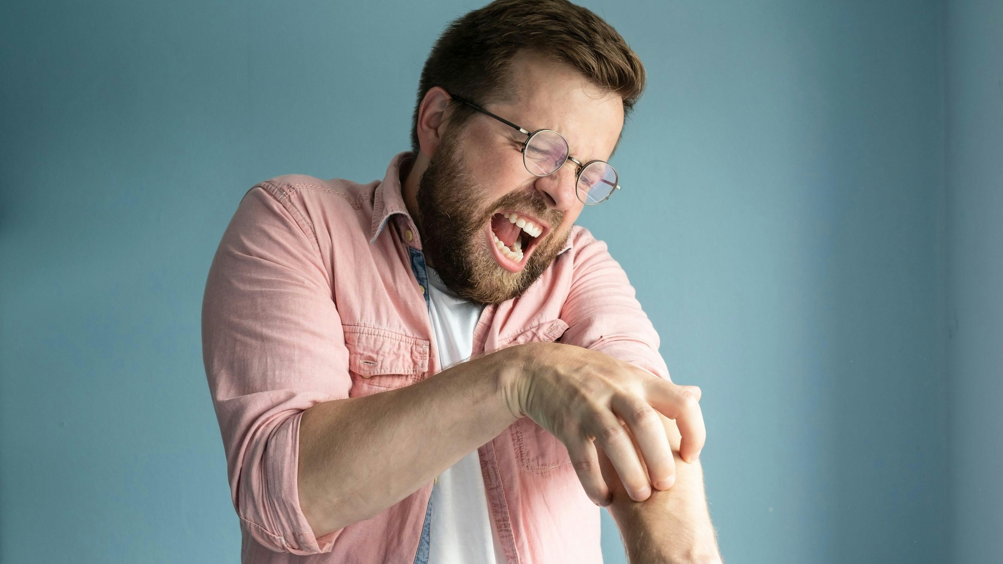a man with glasses is scratching his arm .