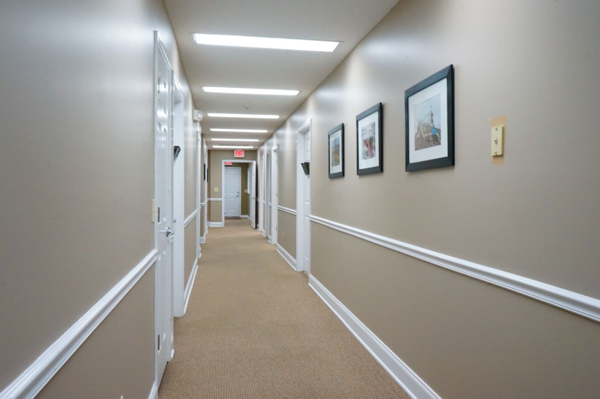 a long hallway with a lot of doors and pictures on the wall at South Georgia Internal Medicine at Swainsboro .