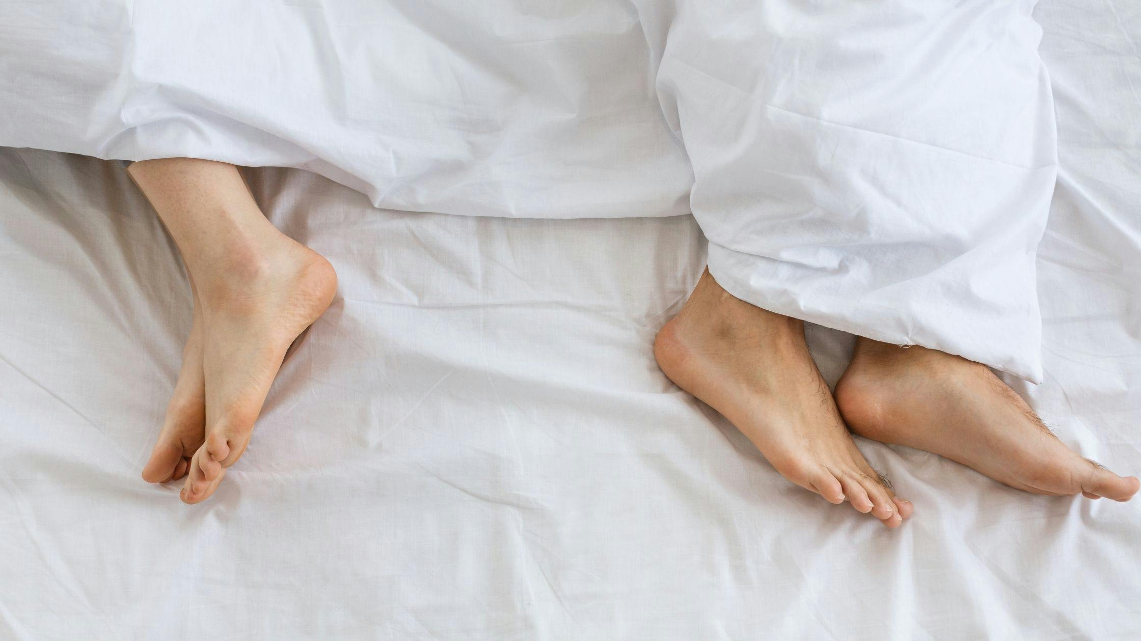 a couple 's feet are sticking out of the blankets on a bed .