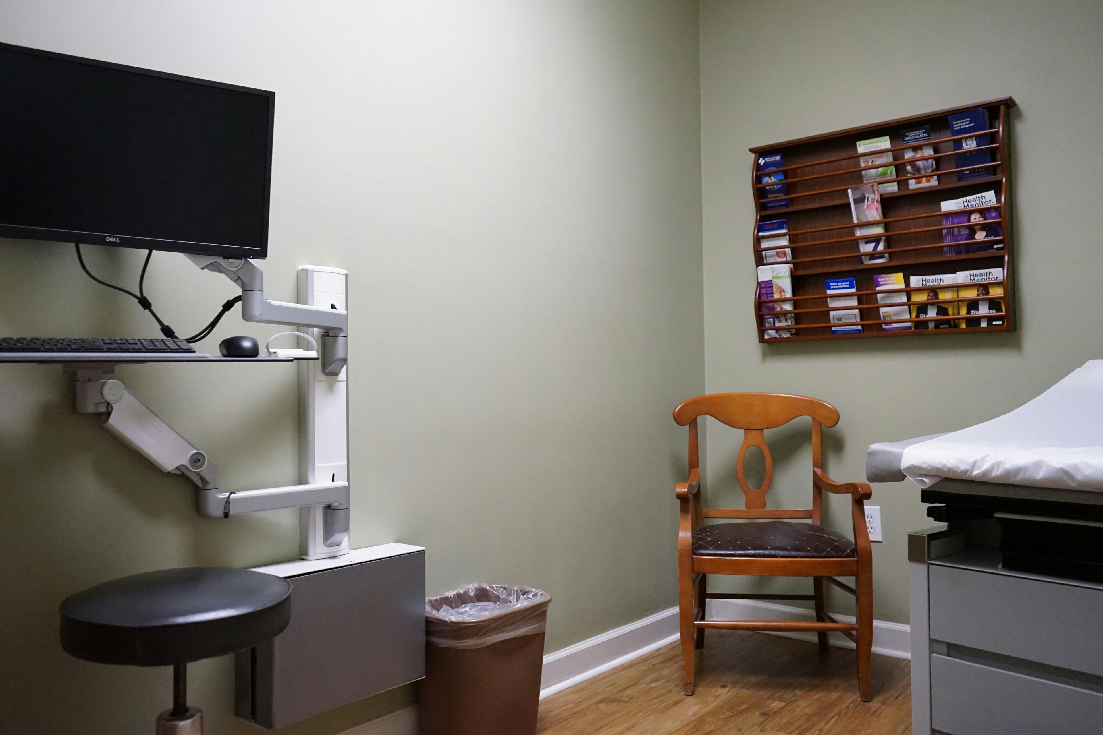 a doctor 's office with a chair , desk , monitor and trash can .