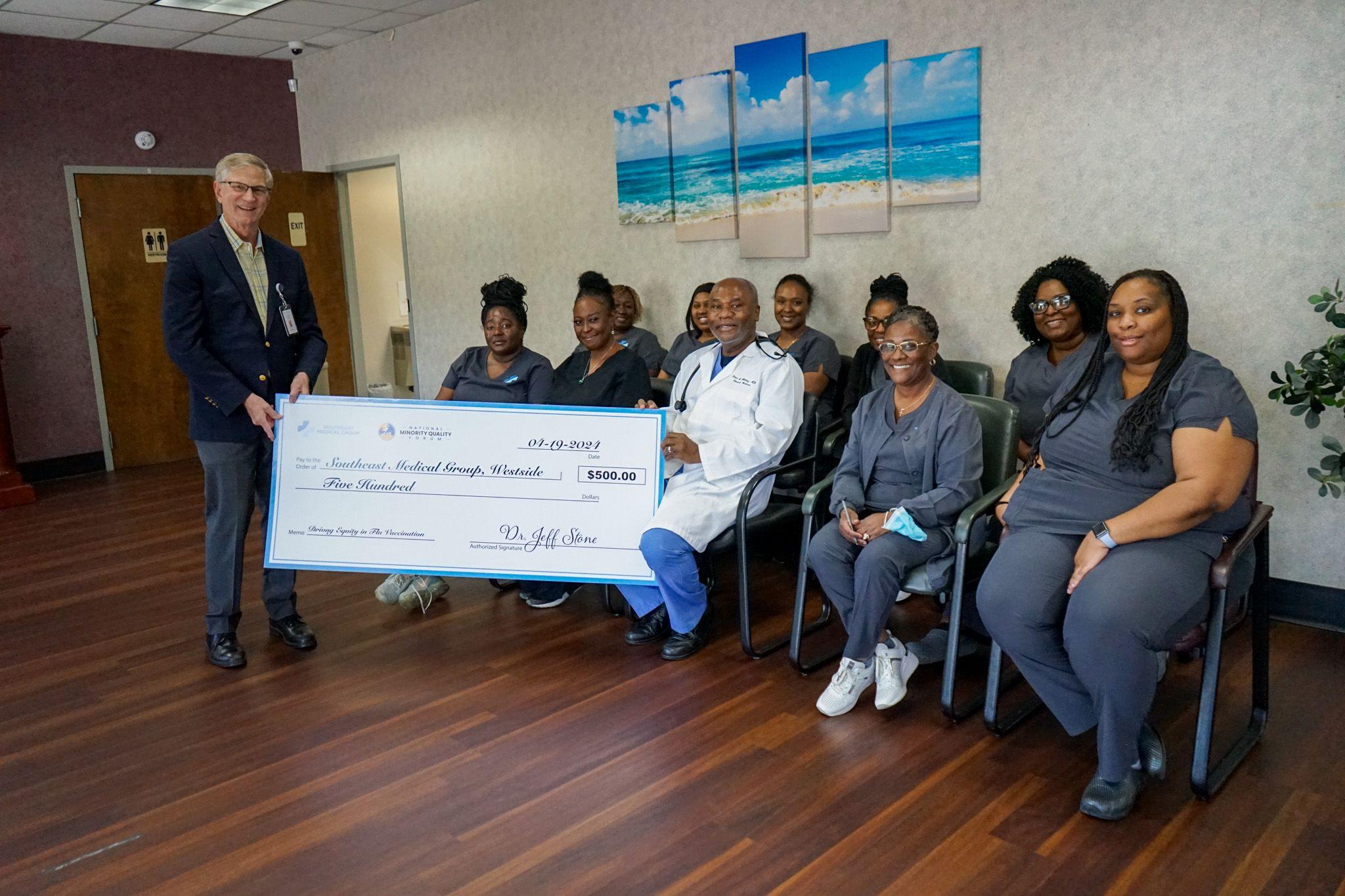 a group of doctors and nurses are sitting in a waiting room holding a large check .