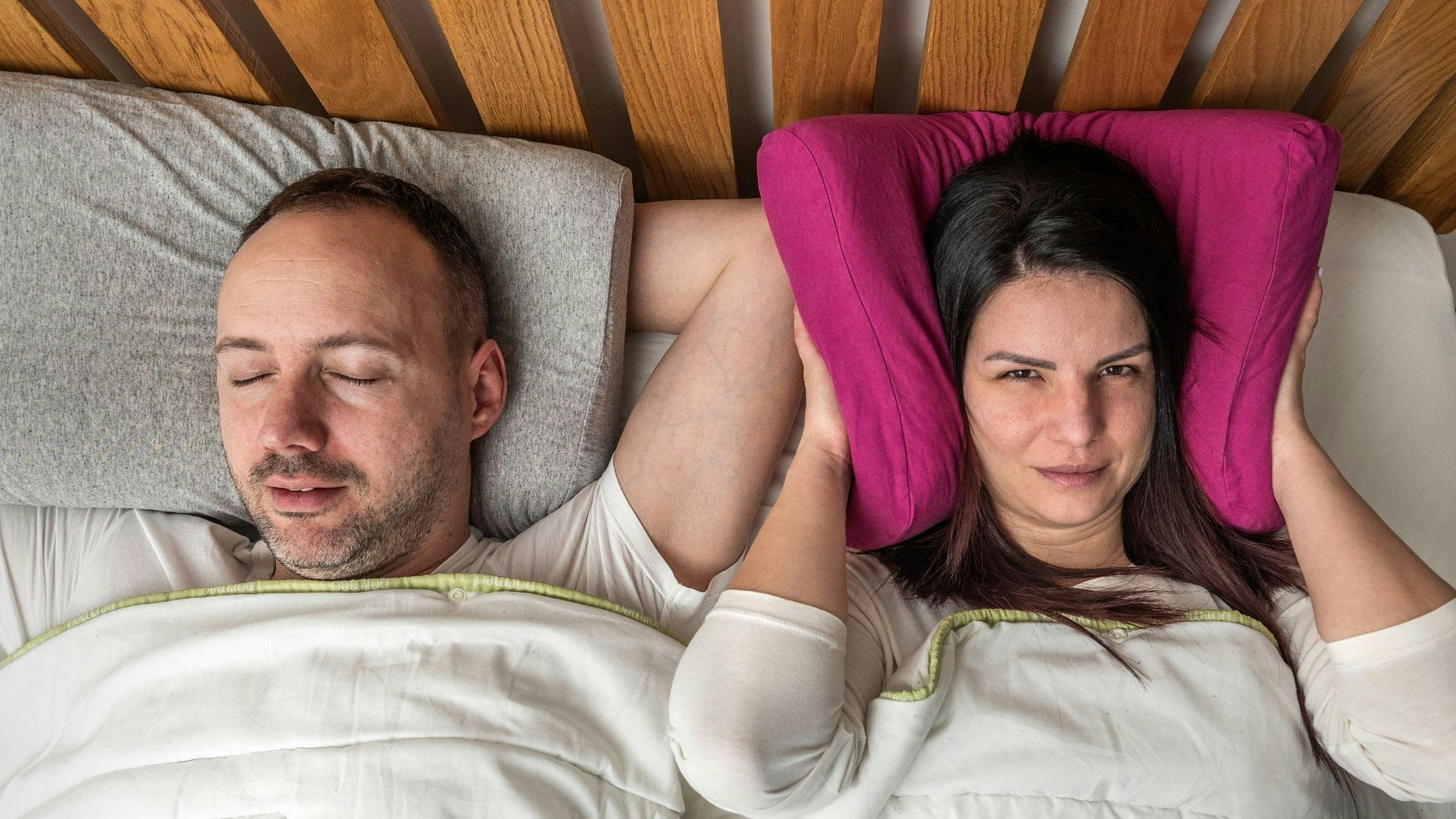 a man and a woman are sleeping in a bed and the woman is covering her ears with a pillow .