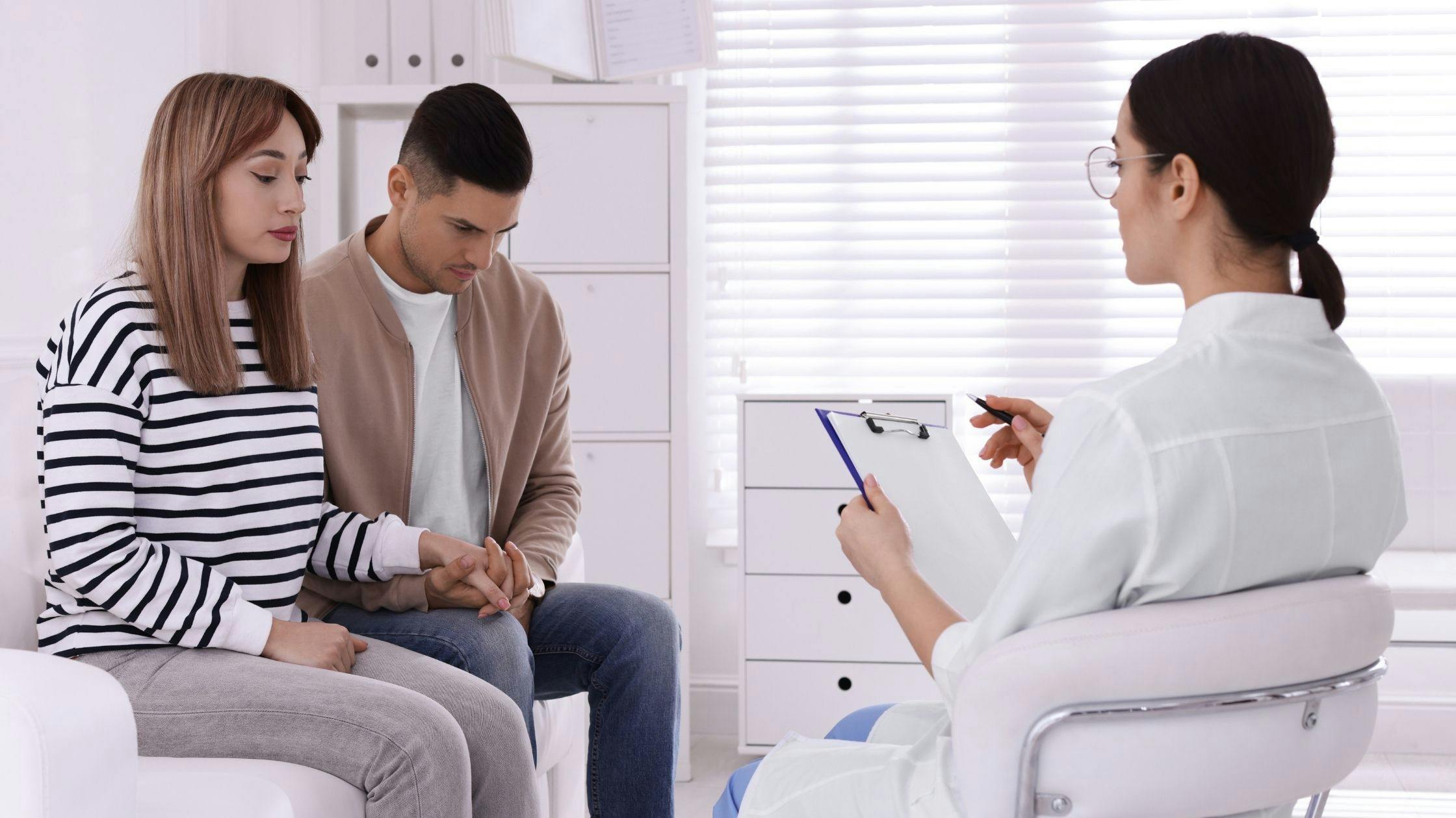 a pregnant woman is sitting next to a man and talking to a doctor .