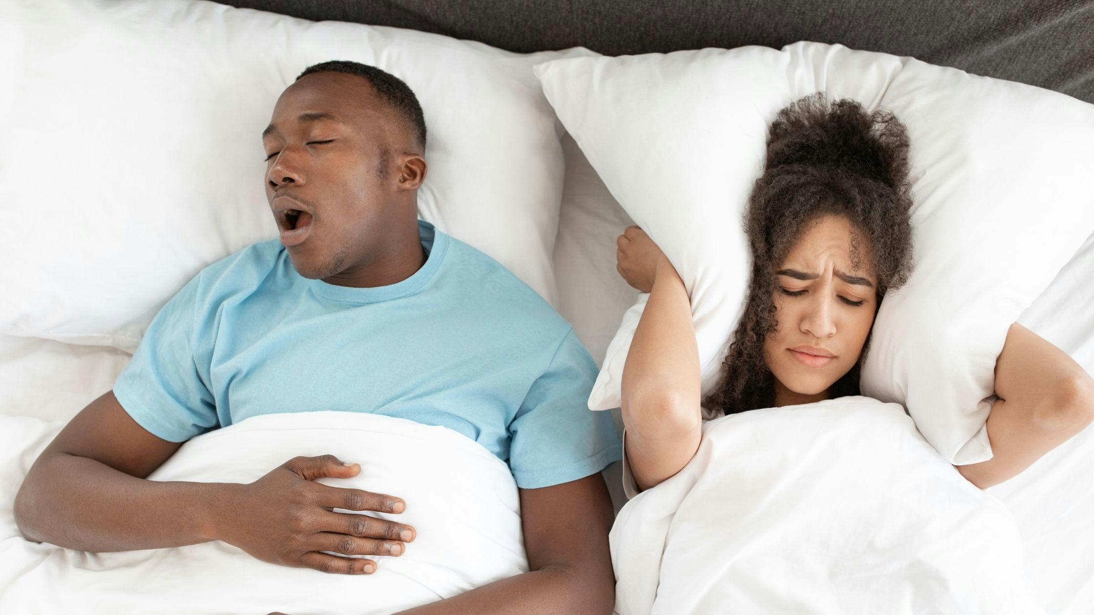 a man is snoring while a woman covers her ears with a pillow .