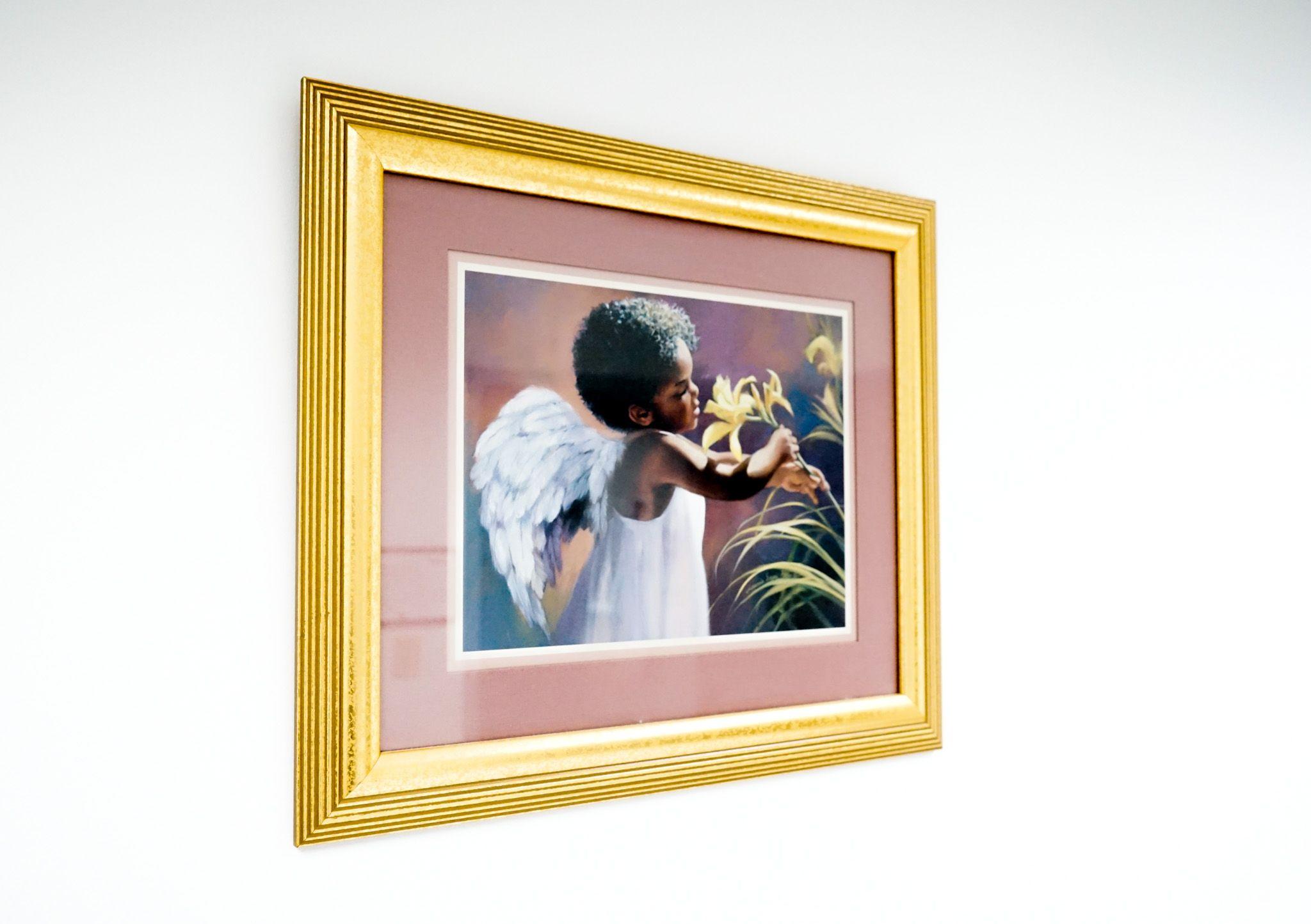 a picture of a child with angel wings holding a flower in a gold frame .