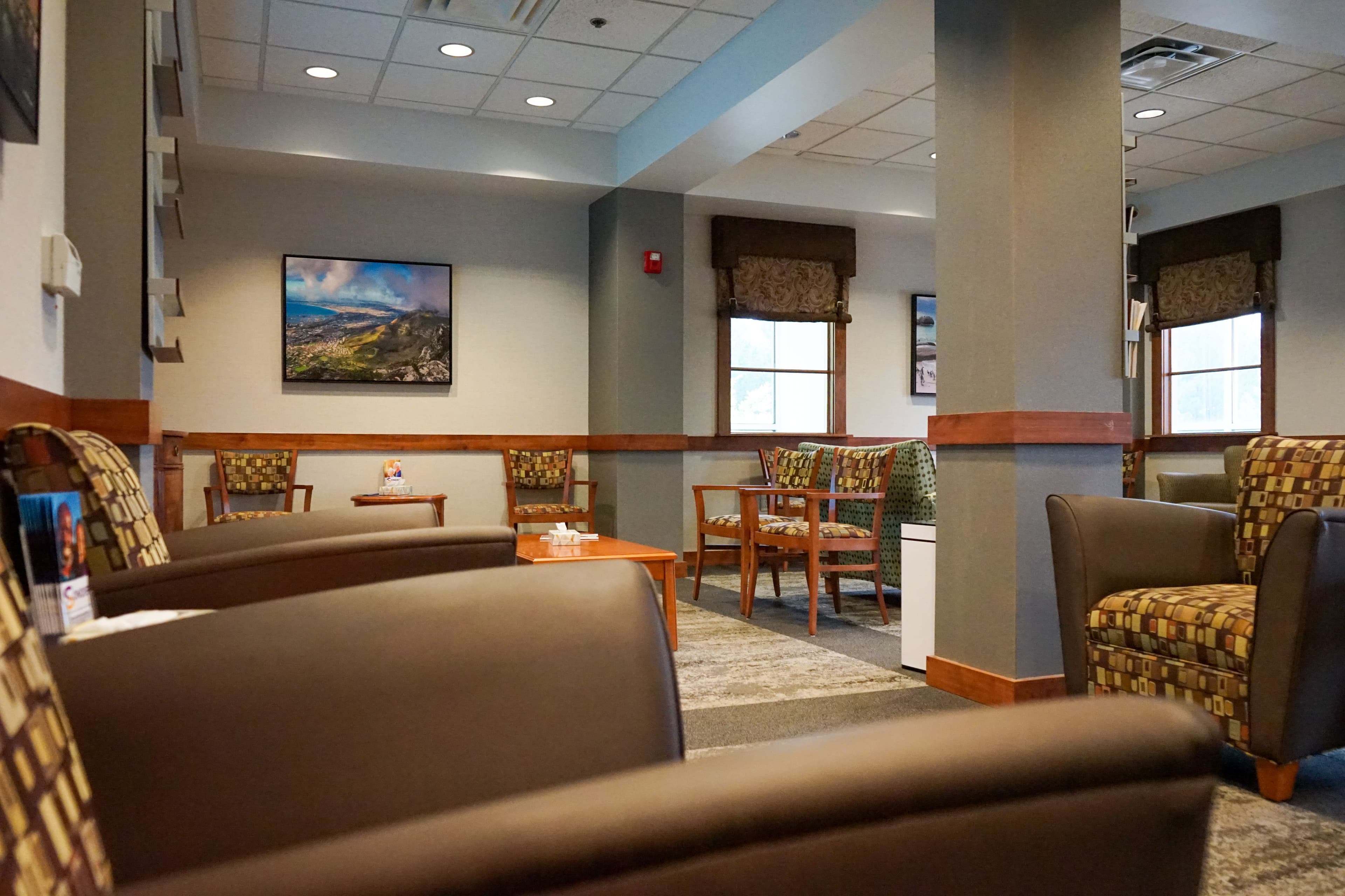 a waiting room with chairs , tables and a painting on the wall .