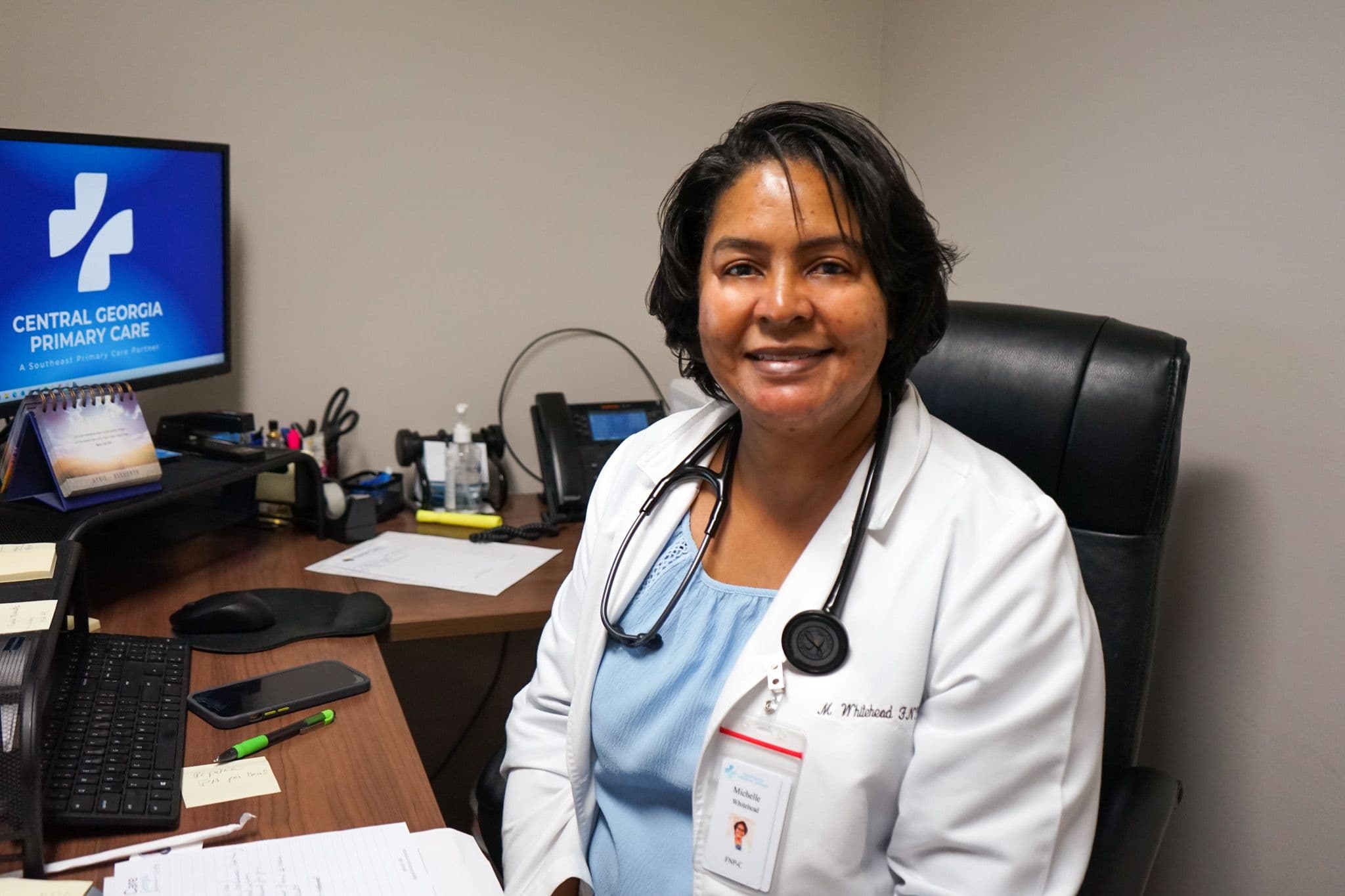 a female doctor is sitting at a desk with a stethoscope around her neck .