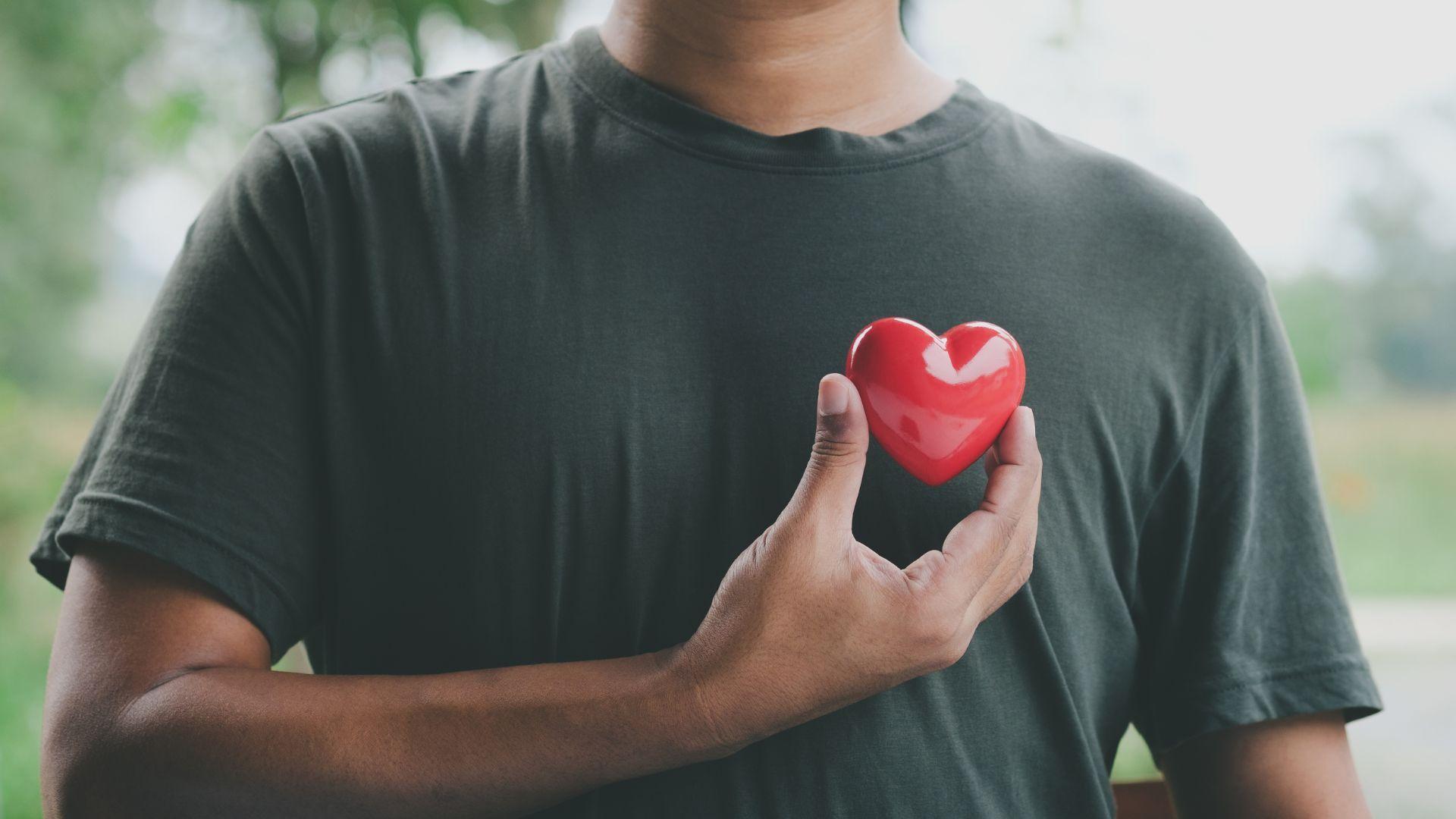 a man is holding a red heart in front of his chest .