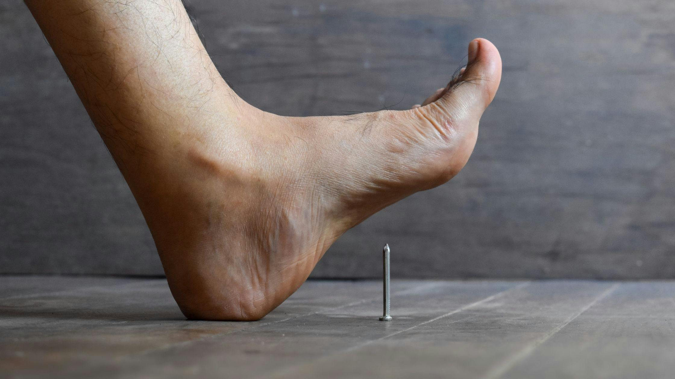 a foot is standing on a nail on a wooden floor .