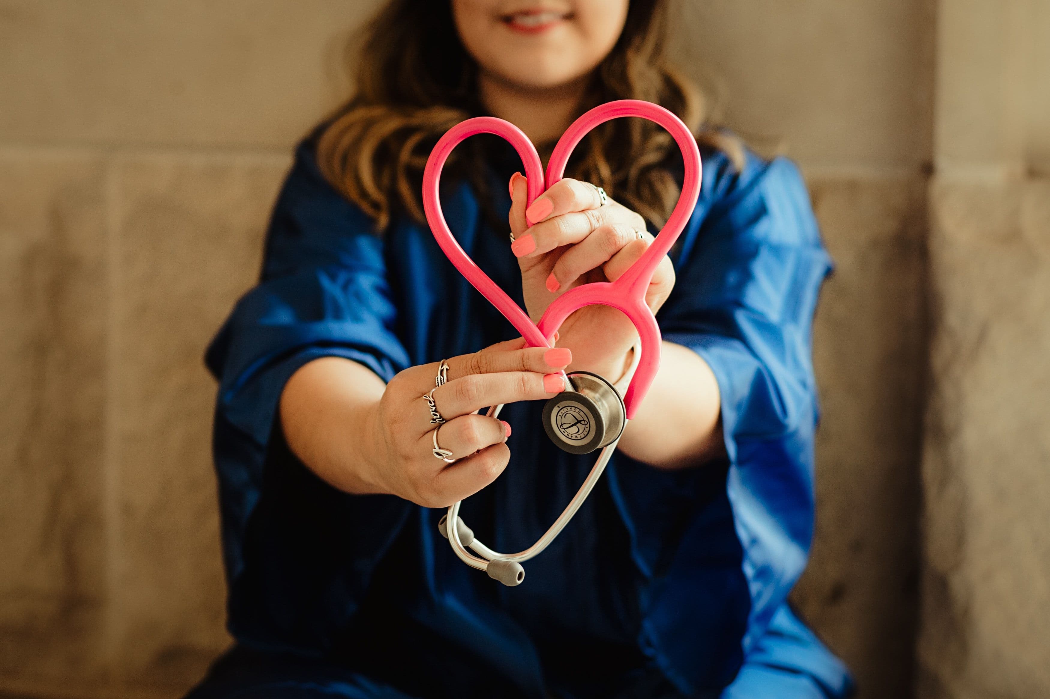 a woman is holding a pink stethoscope in the shape of a heart .