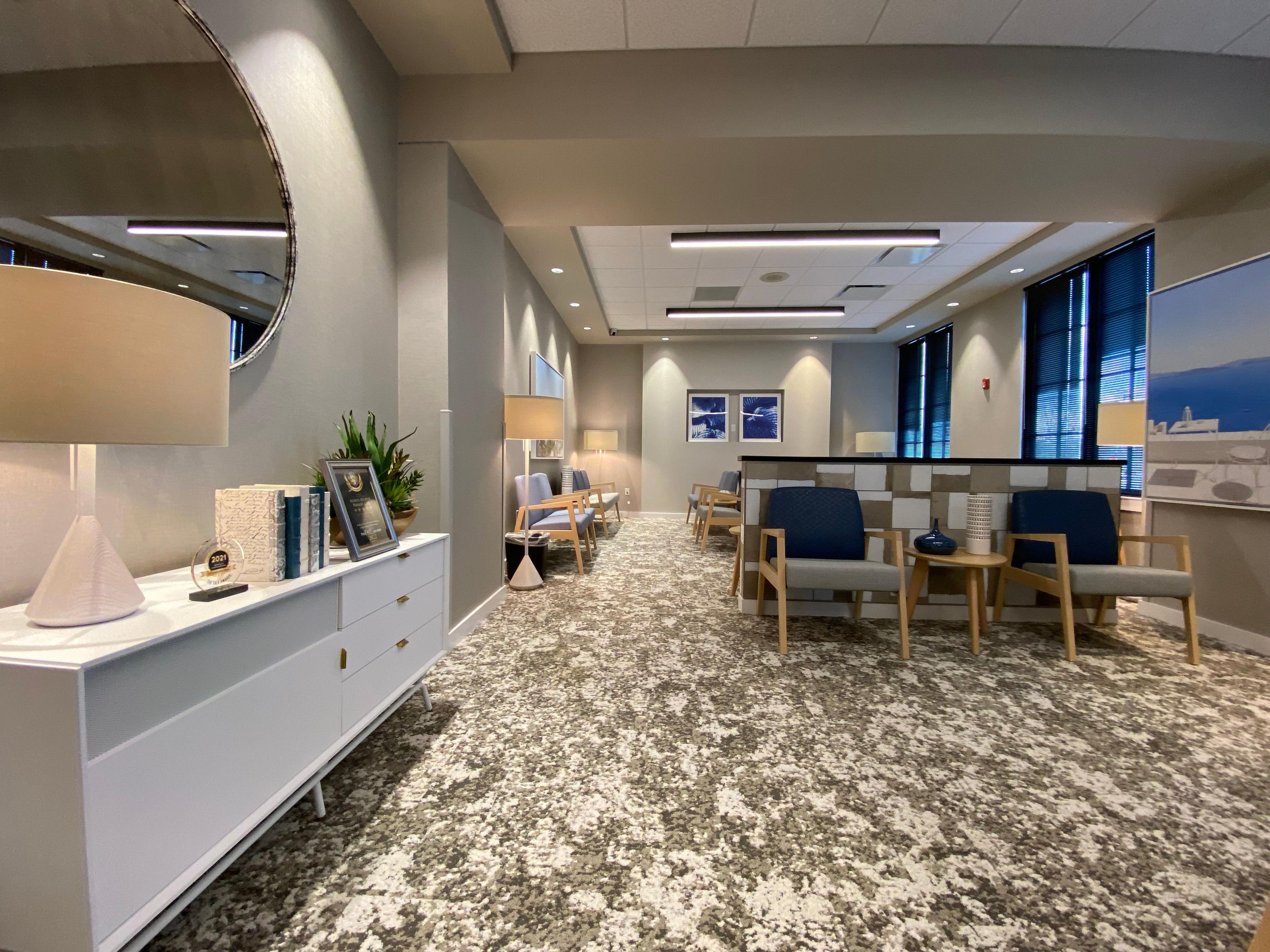 a waiting room with chairs , tables , lamps and a mirror .