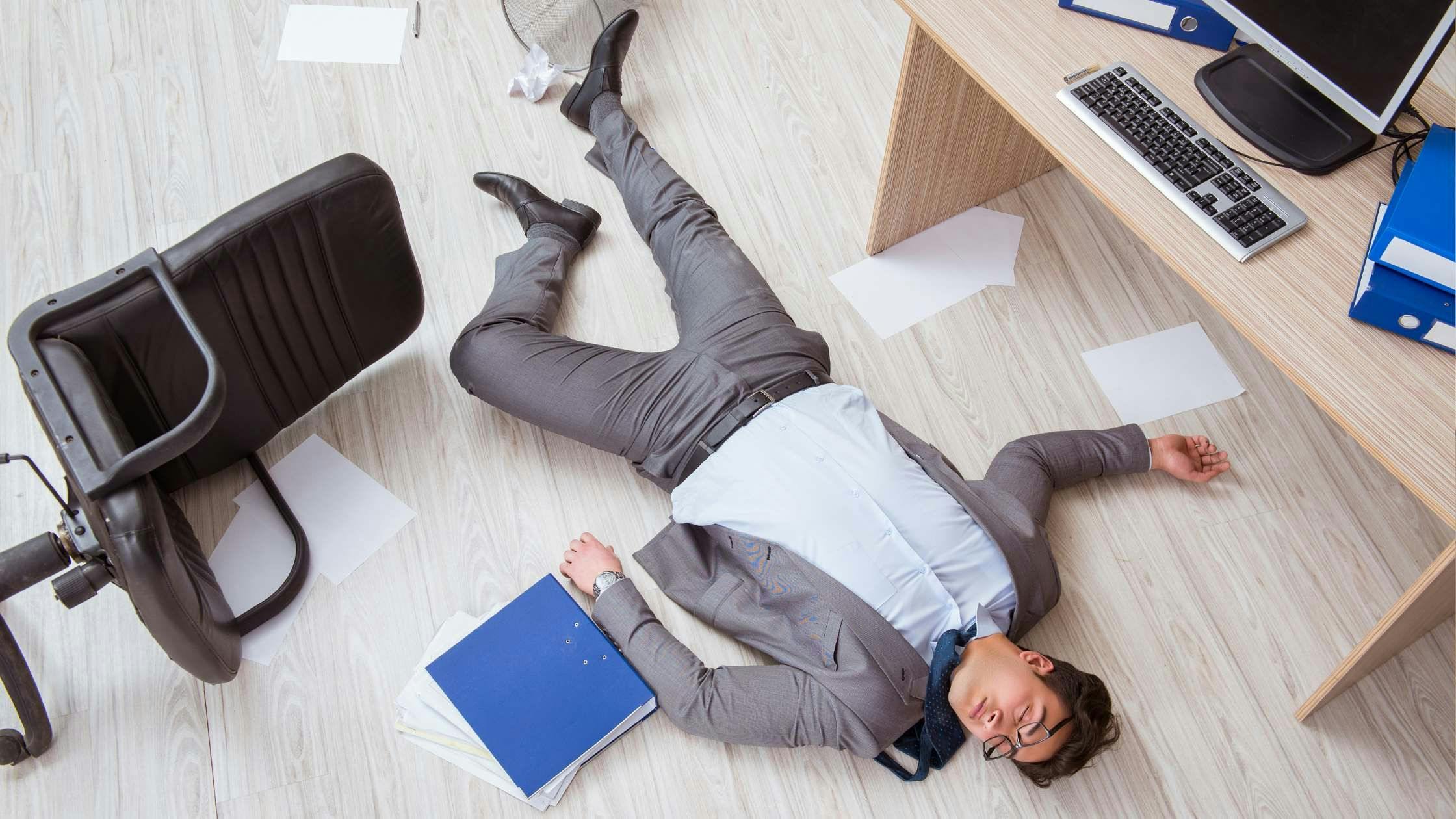 a man is fainted and laying on the floor in an office .
