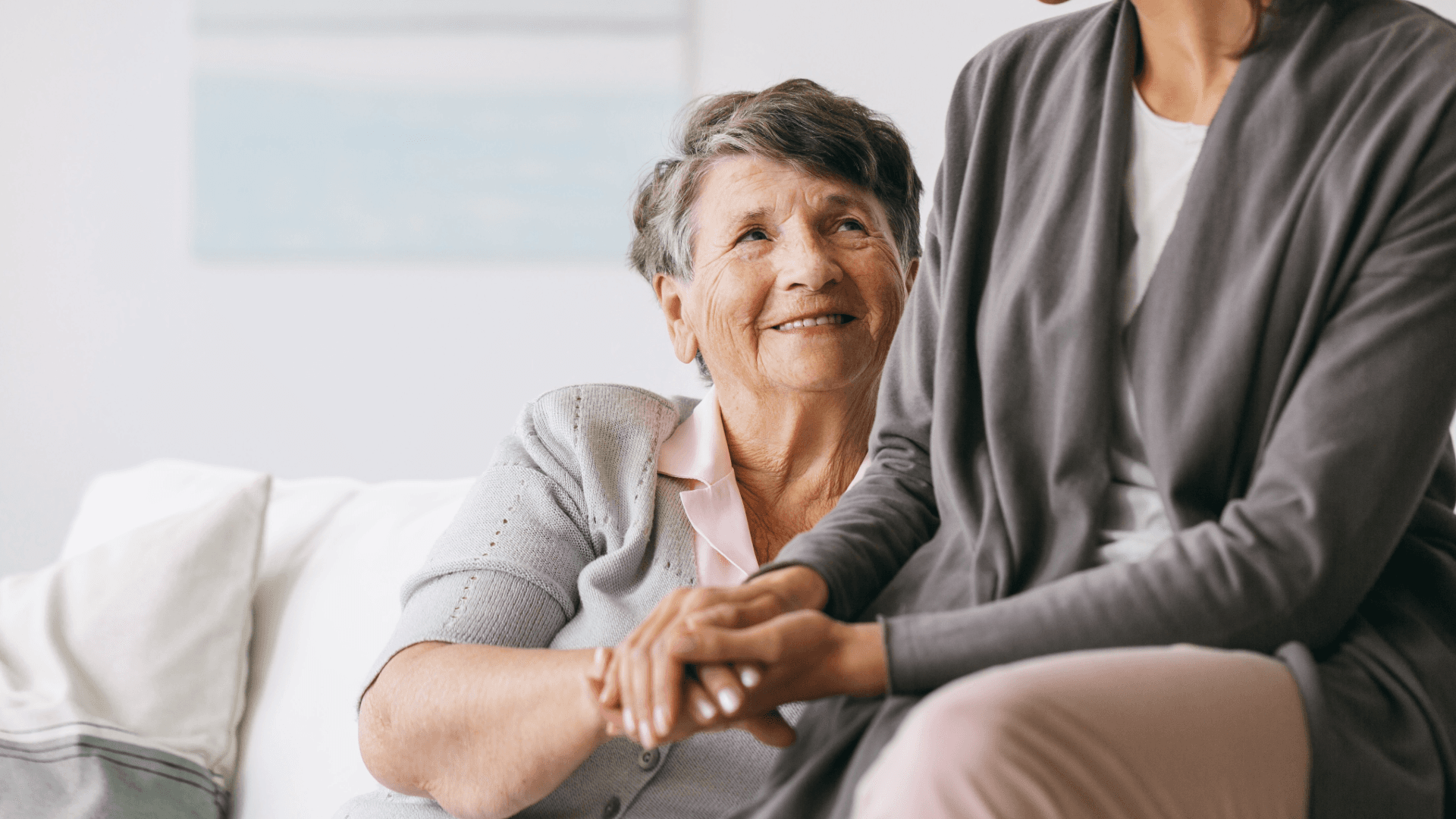 Alzheimer's Awareness: an elderly woman sits on a couch holding hands with a younger woman