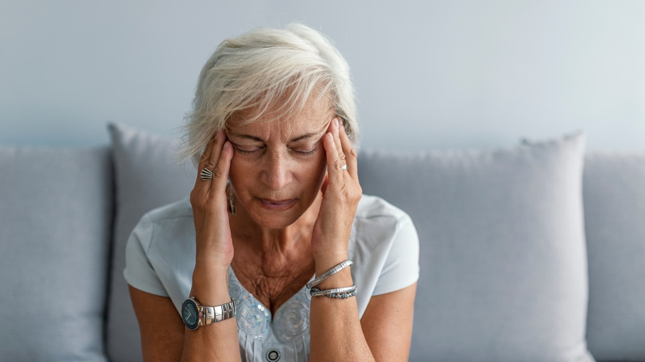 an older woman is sitting on a couch with her hands on her head .