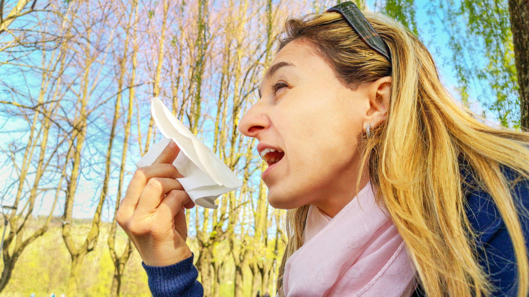 a woman is blowing her nose with a napkin in a park .