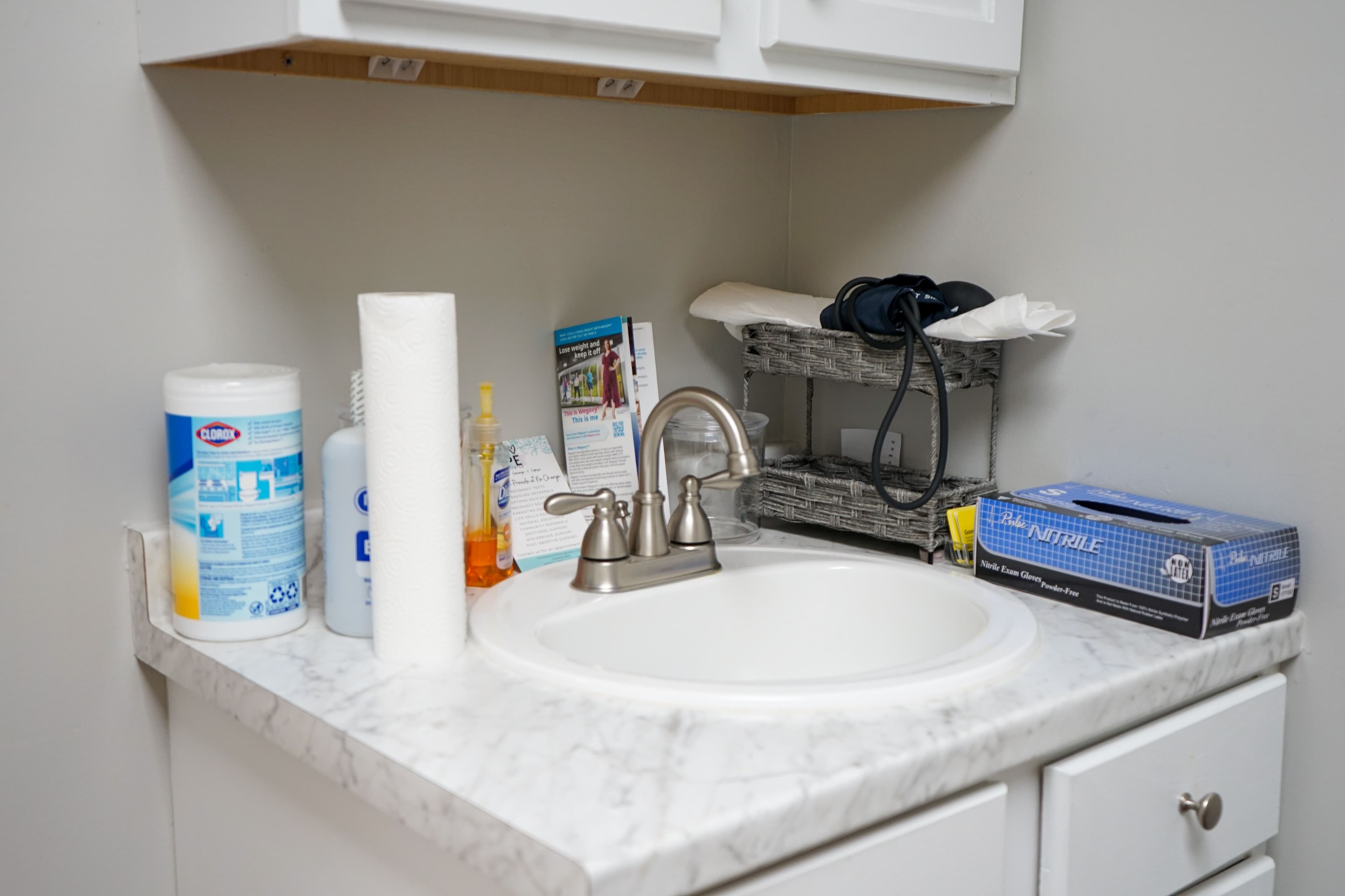 a bathroom sink with a faucet , paper towels , and gloves on the counter .