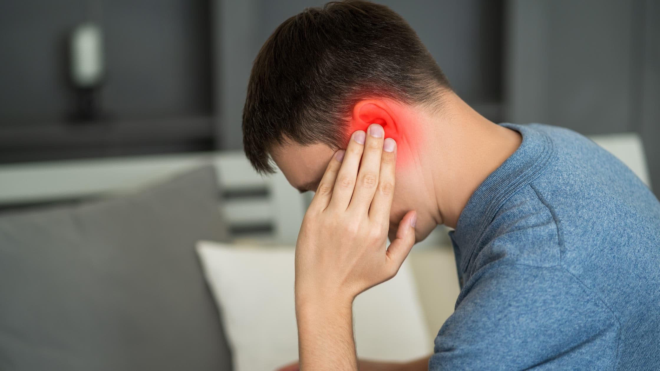 a man is sitting on a couch holding his ear in pain .