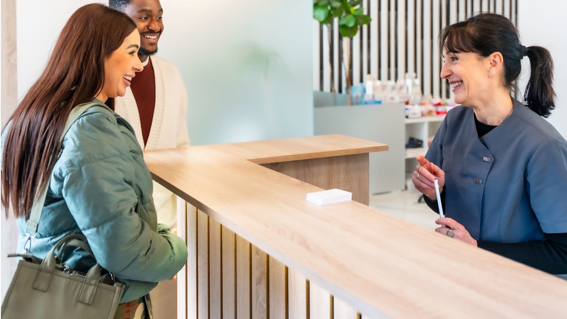 Two smiling patients at a reception desk interacting with a smiling staff from Southeast Medical Group.
