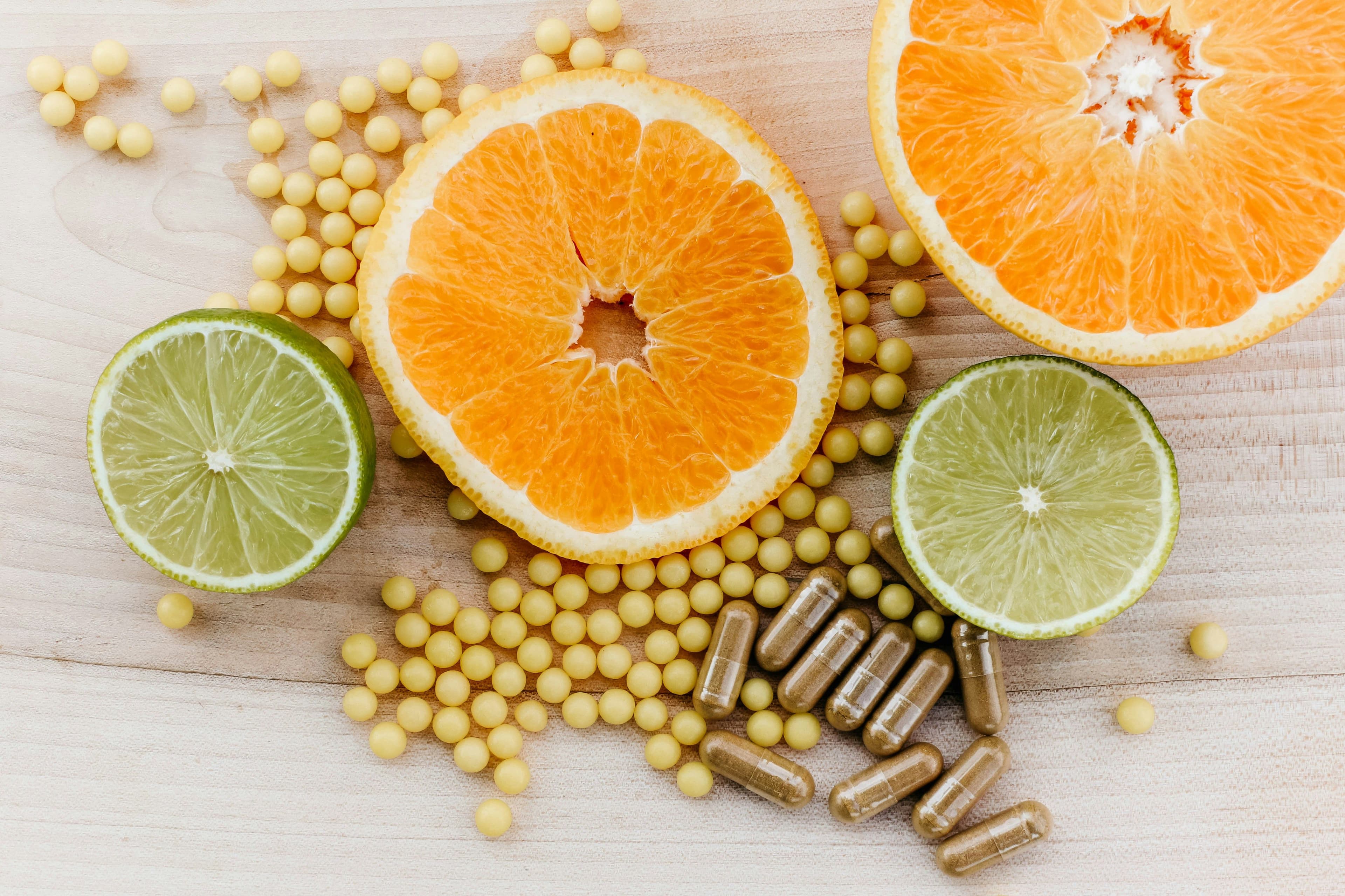 an orange , lime , and pills are on a wooden table .