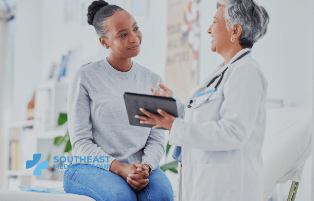 A smiling patient listens to a doctor holding a tablet in a medical office.
