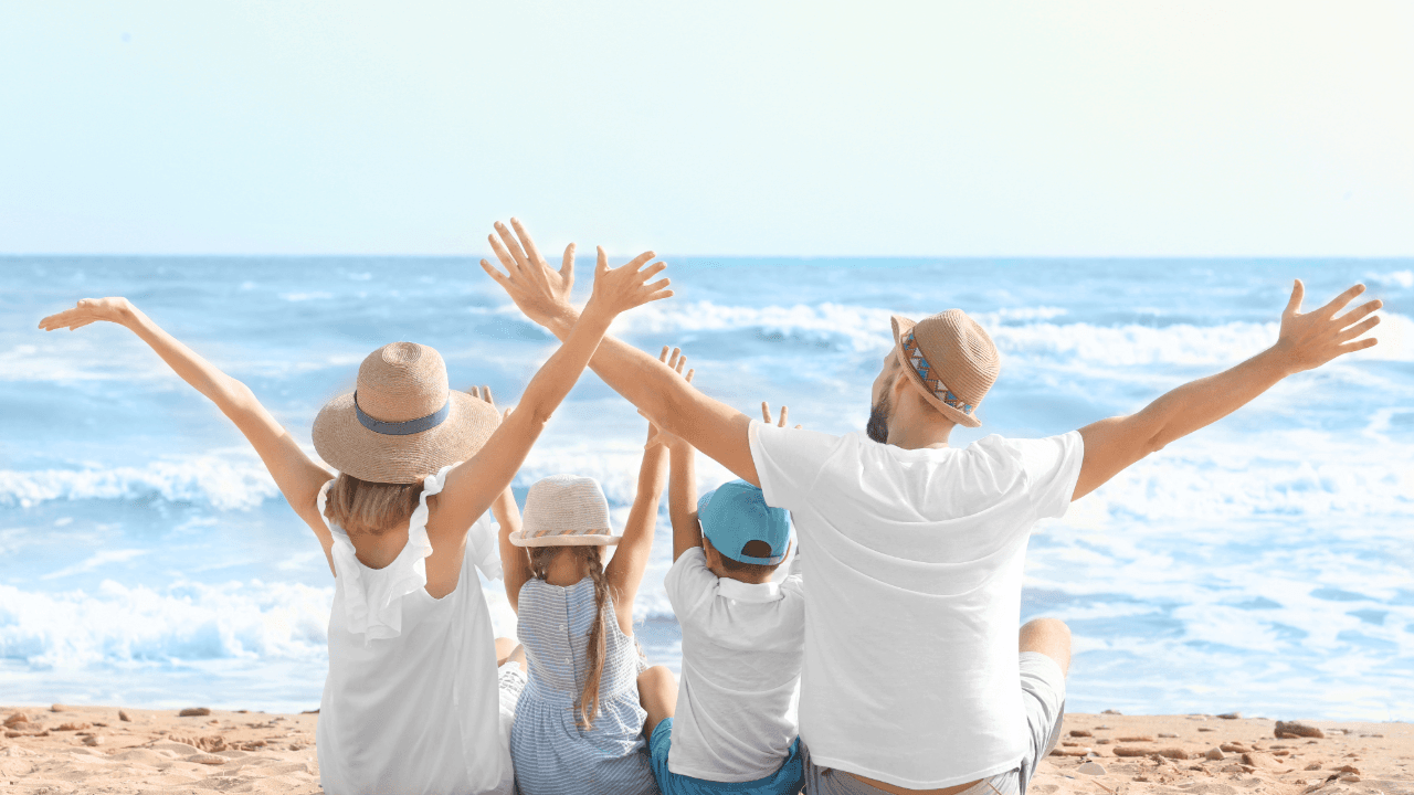 Family Holiday: a family sits on the beach with their arms outstretched