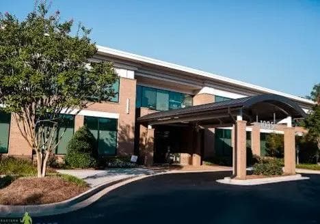 Modern brick building with a covered entrance marked "1035," large windows, and surrounding greenery under a blue sky. Primary Care at Stockbridge