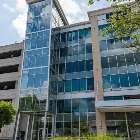 A modern glass building reflecting a cloudy sky, with an adjacent concrete parking garage.