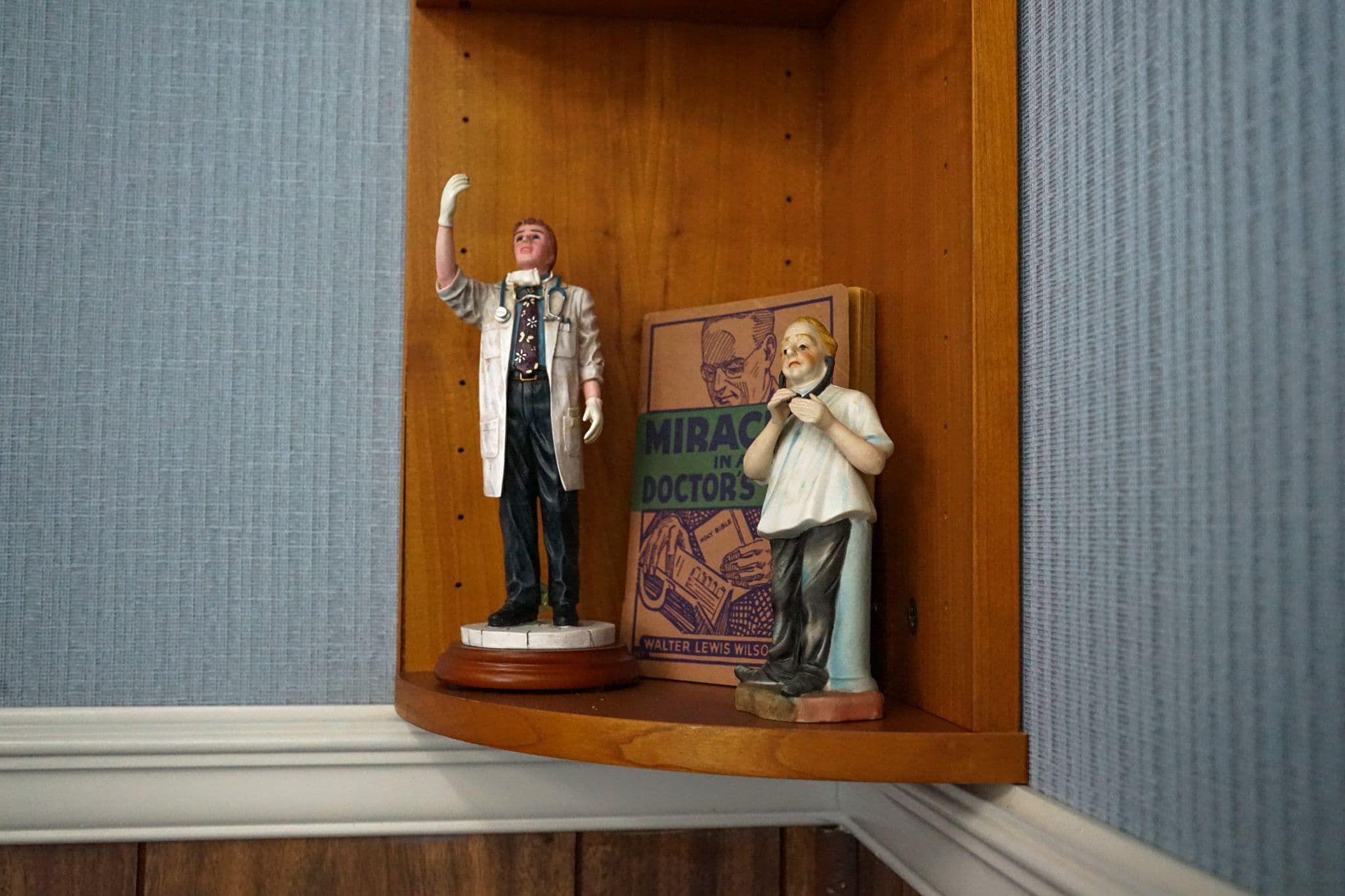 two figurines of doctors are sitting on a shelf next to a book .