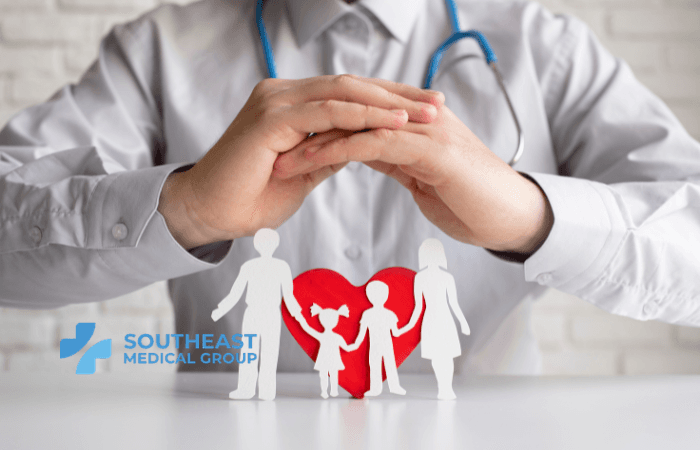 Doctor's hands protecting paper figures of a family and a red heart, with the Southeast Medical Group logo.