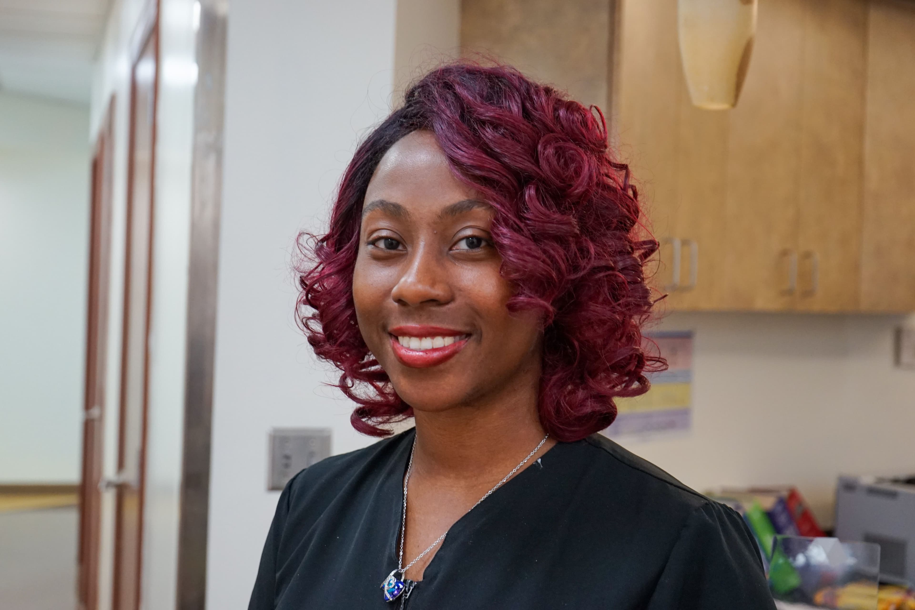 a woman with red hair is wearing a black scrub top and smiling for the camera .