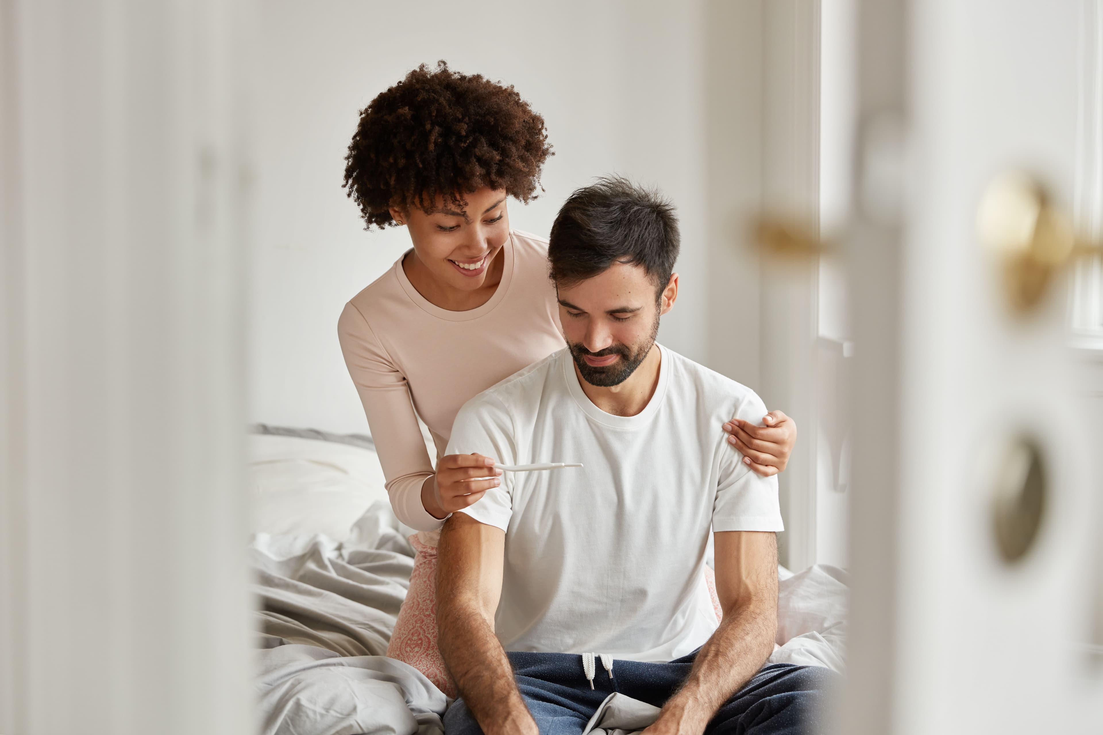 World Sexual Health Day: a woman is holding a pregnancy test next to a man sitting on a bed .