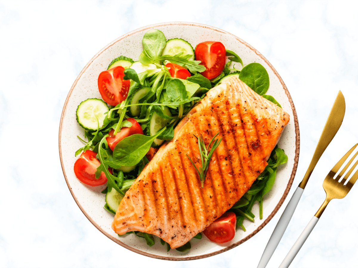 Grilled salmon with rosemary, a fresh salad of greens, cucumber, and tomatoes, served with gold flatware.