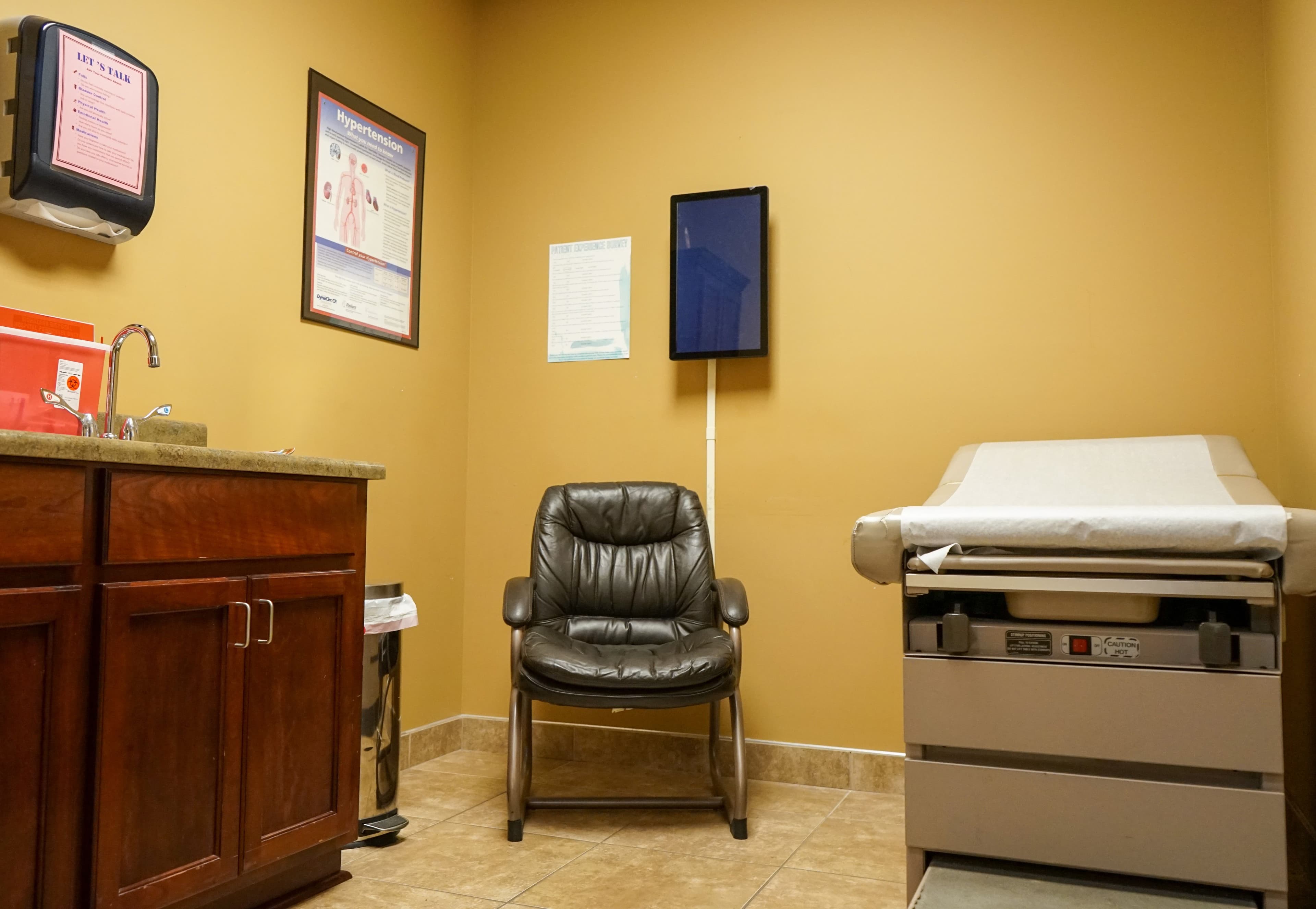 a doctor 's office with a chair , examination table and sink .