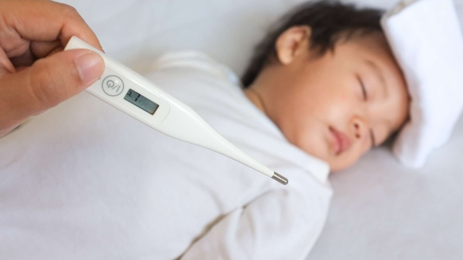 a person is holding a thermometer over a baby 's head .