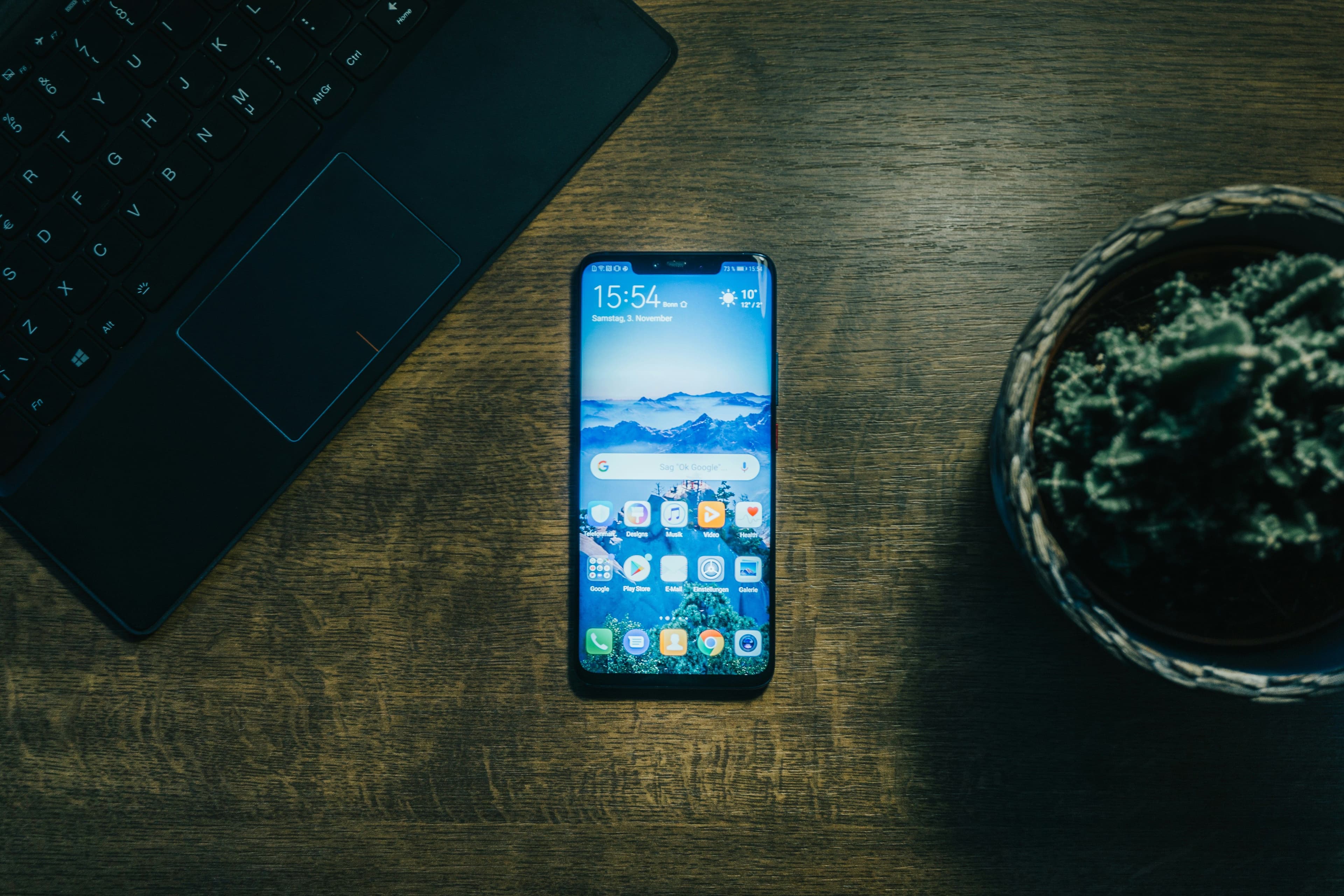 a cell phone is sitting on a wooden table next to a laptop and a potted plant .