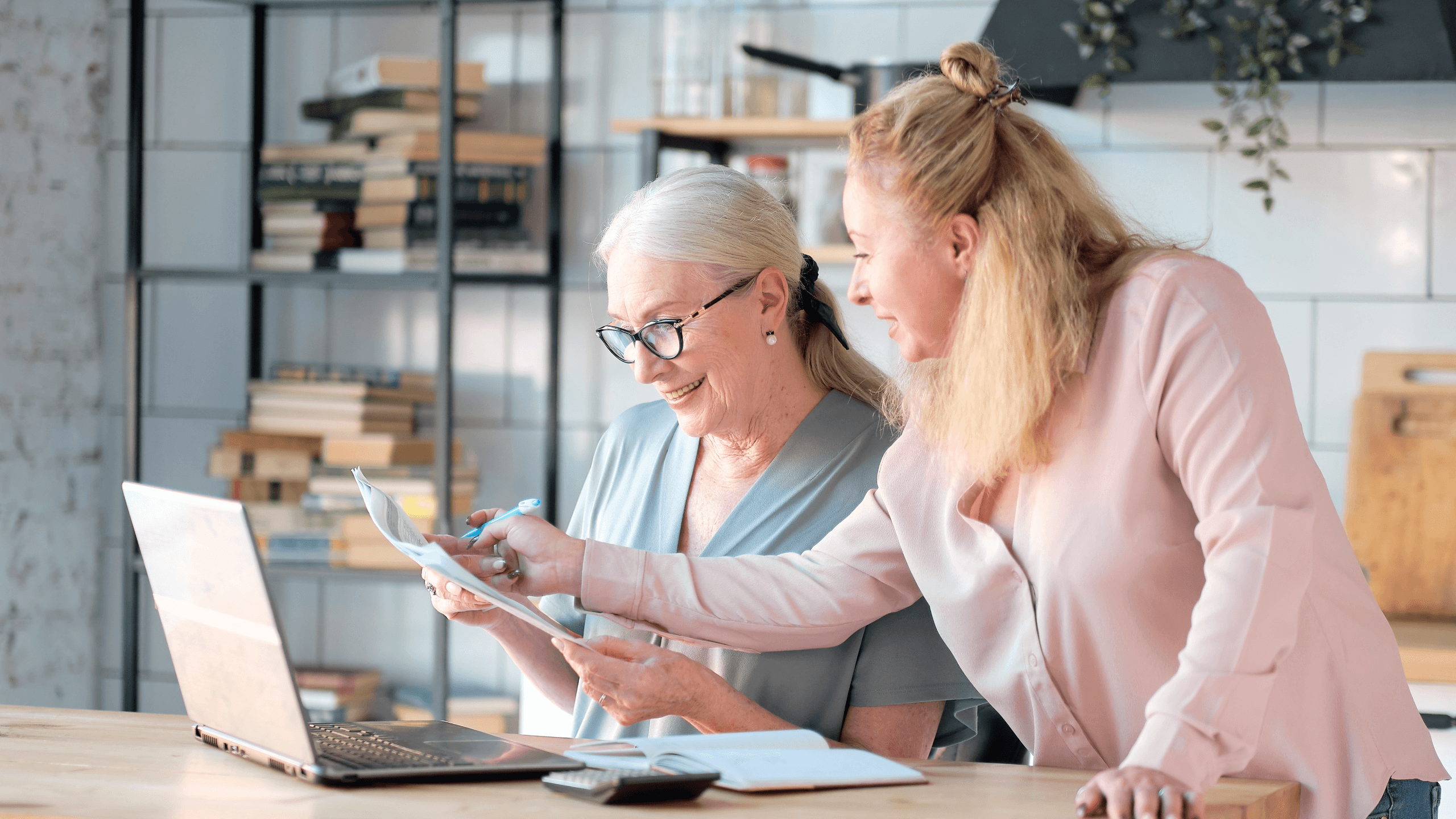 two women are looking at a laptop and a piece of paper