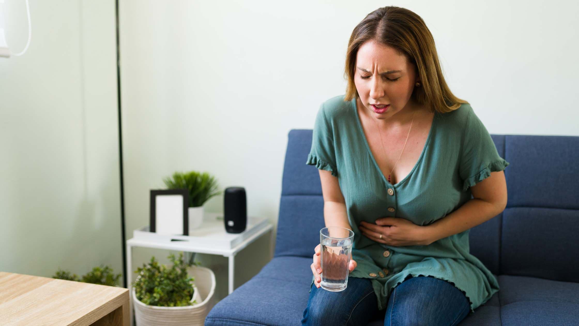a woman is sitting on a couch holding a glass of water .