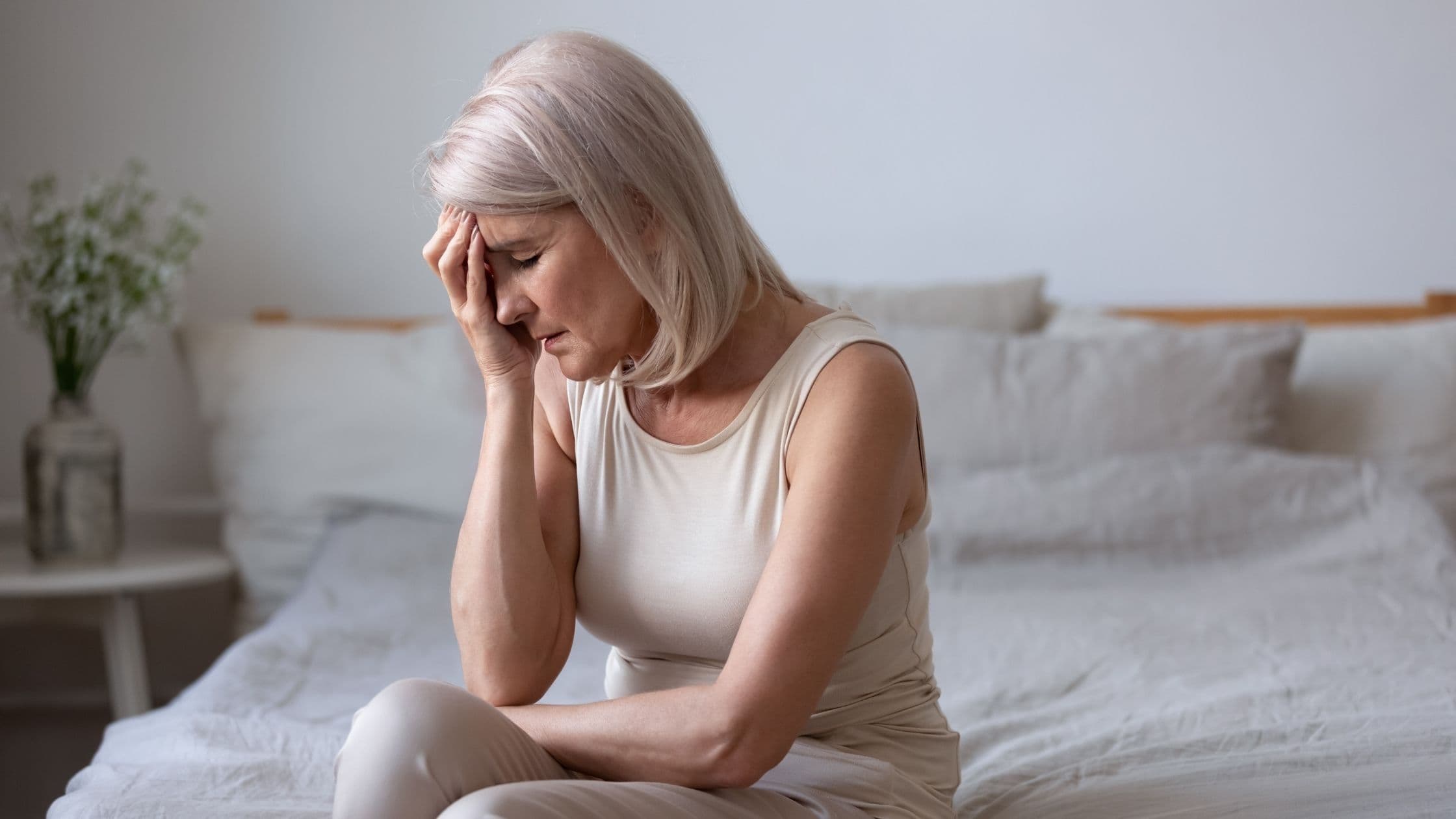 an older woman is sitting on a bed with her head in her hands .
