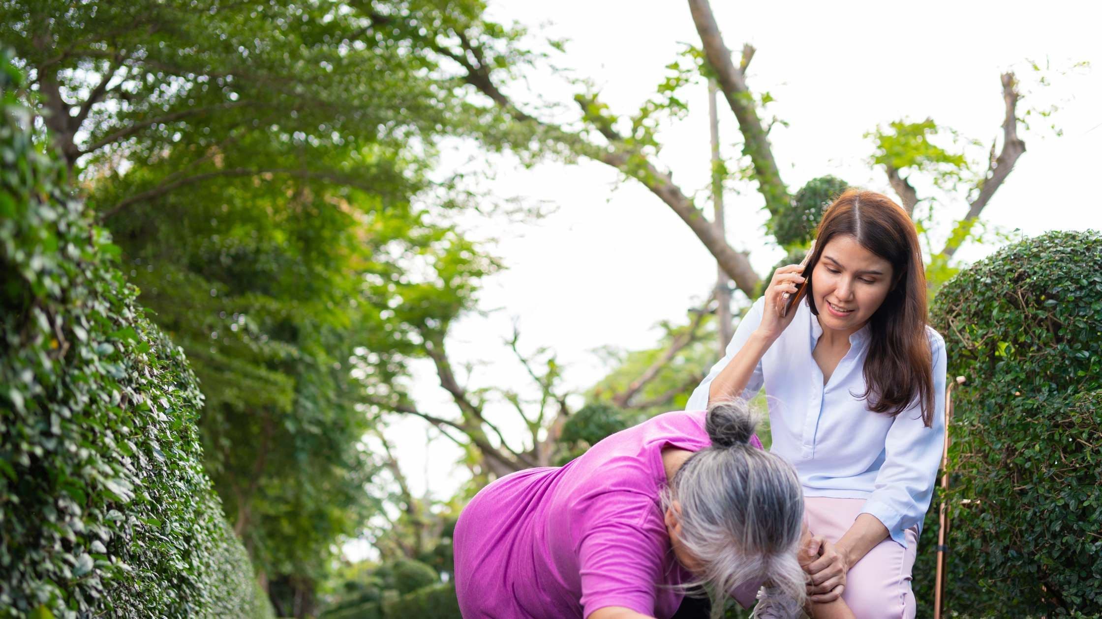 a woman is kneeling down next to an older woman who is talking on a cell phone .