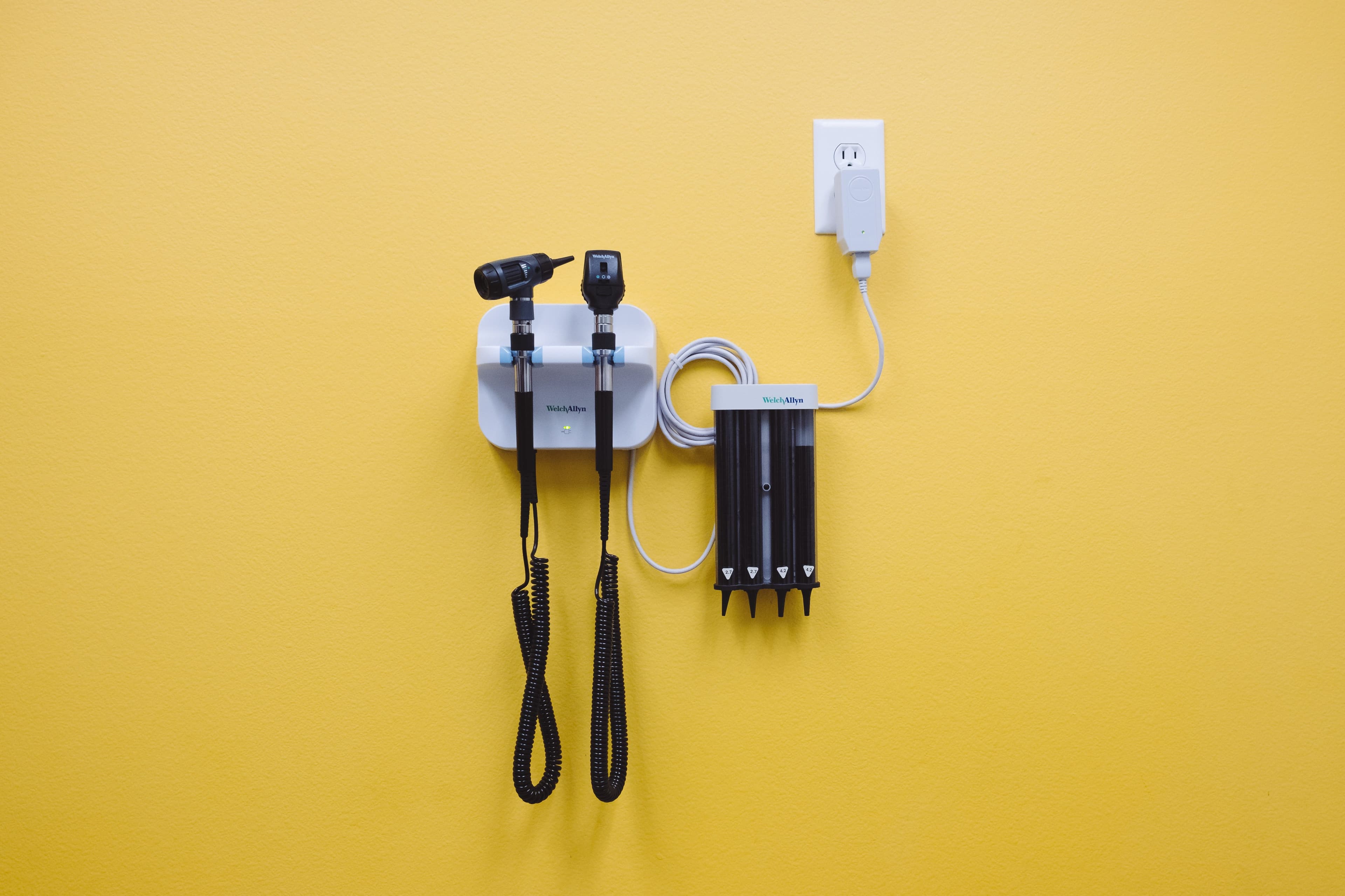 a pair of stethoscopes hanging on a yellow wall next to a charger .