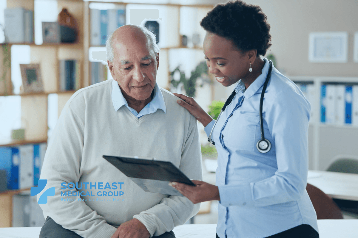 A female doctor with a stethoscope comforts an older male patient while they review a clipboard.
