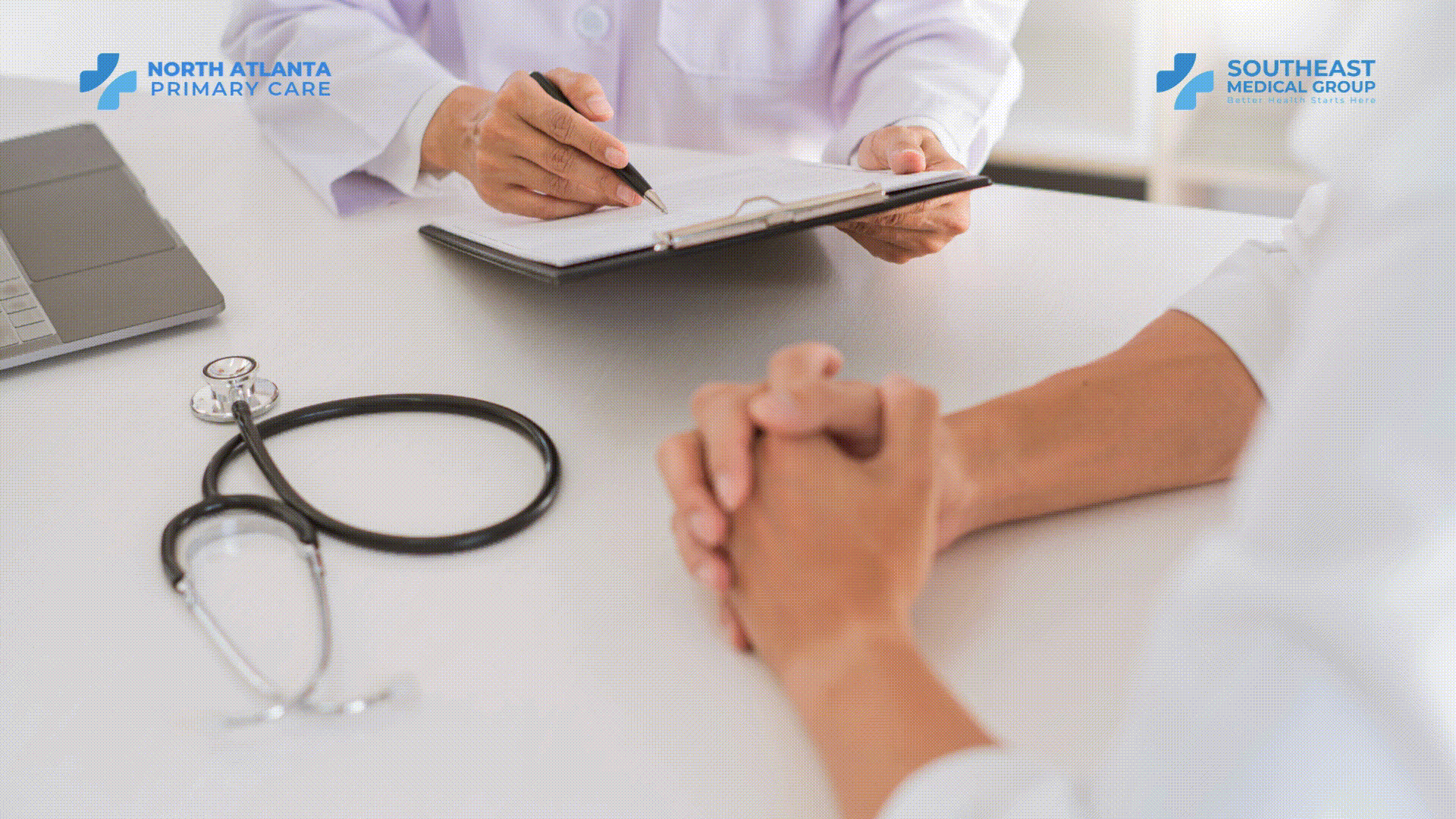 Doctor writing on a clipboard during a patient consultation; a stethoscope is on the table.