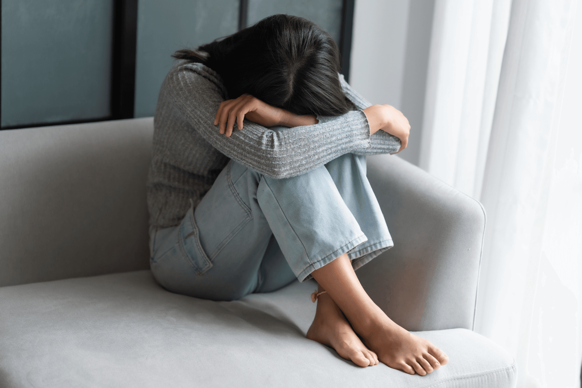 Surviving Holiday Stress: A person sits curled up on a sofa, head buried in their arms.