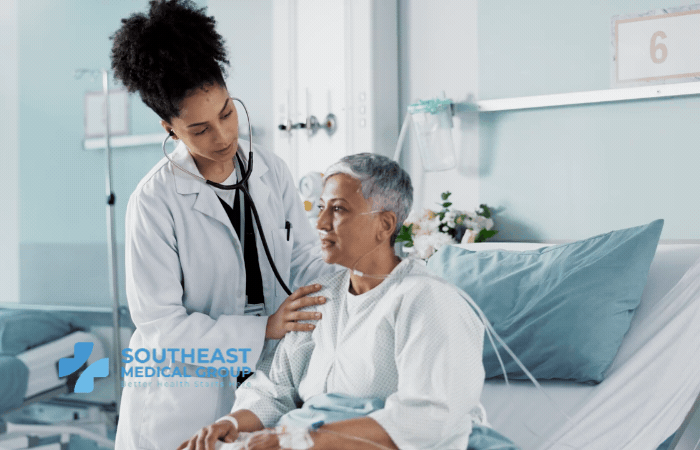 A female doctor uses a stethoscope to examine an older female patient in a hospital room.